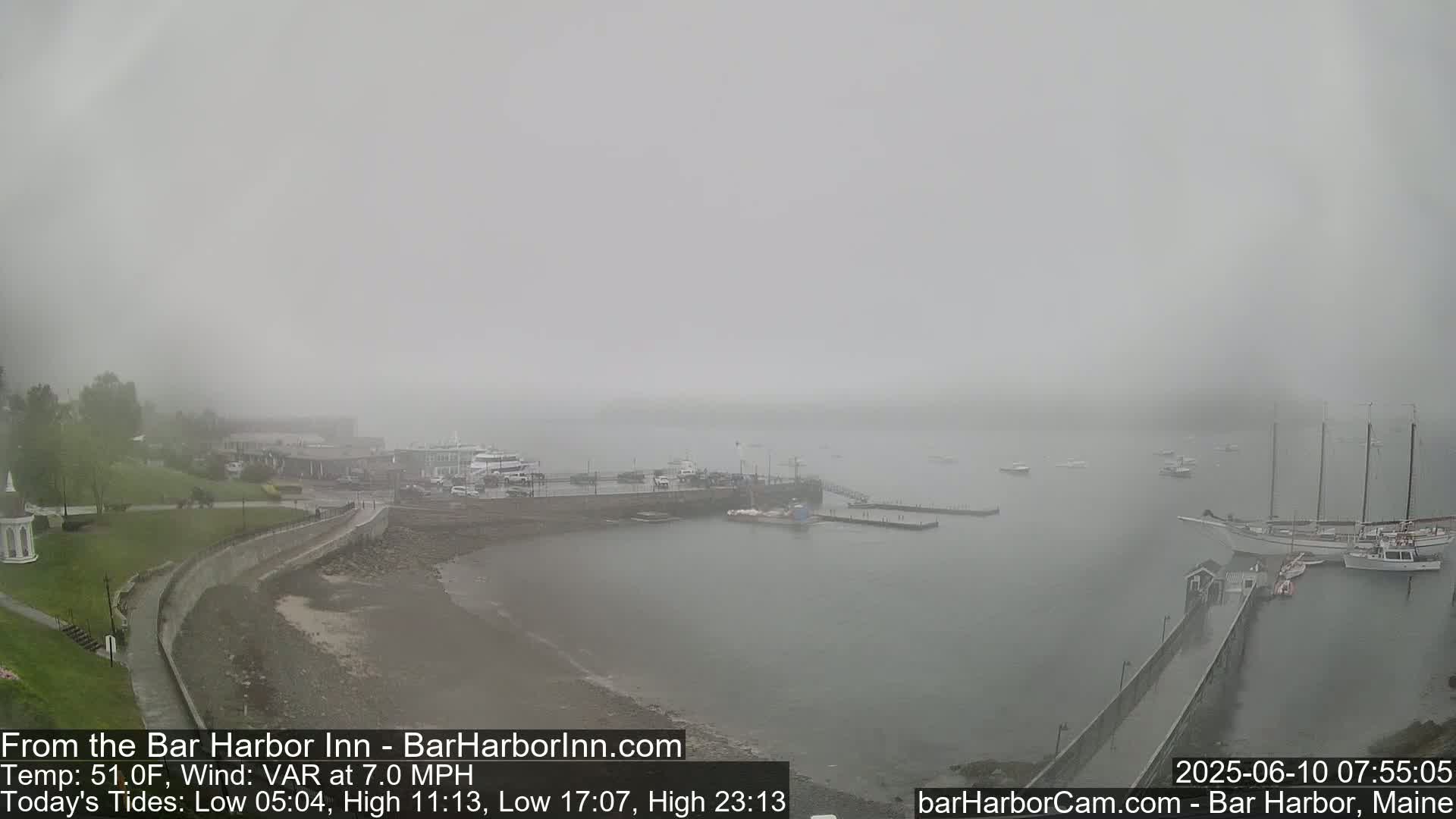 A foggy harbor scene shows a shoreline with docked boats and a walkway leading to a pier, with buildings visible in the distance.