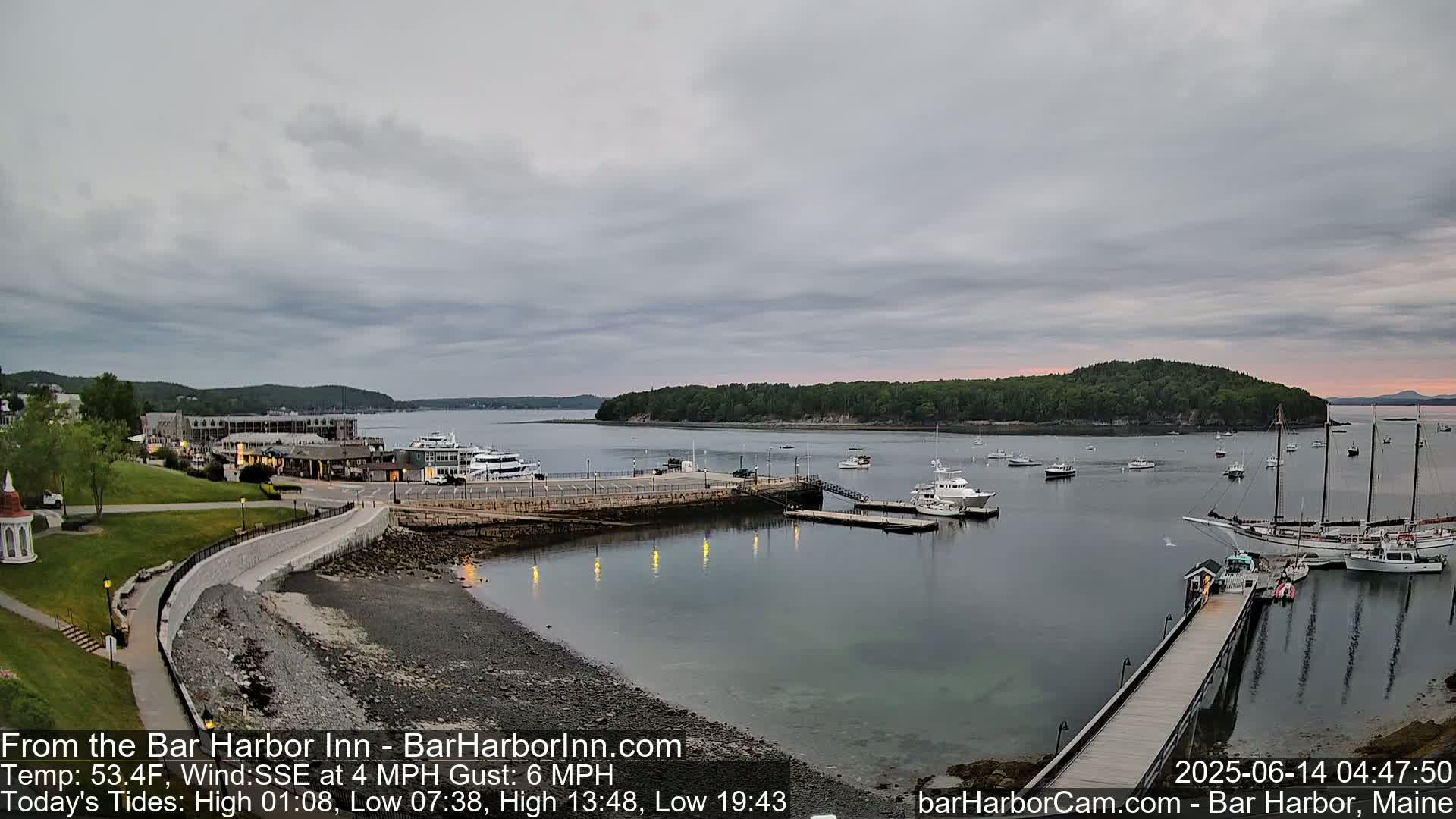 A calm harbor with numerous boats and a waterfront building under an overcast sky.