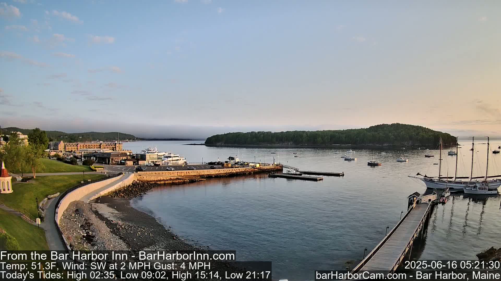 A calm harbor scene at sunrise, with boats docked and anchored, a hotel in the background, and a light fog over the water.