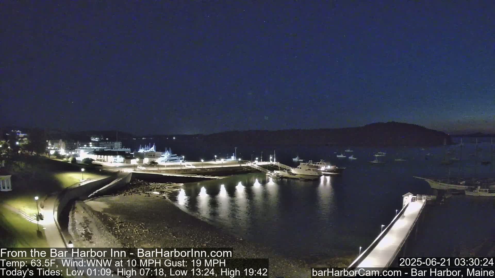 A nighttime harbor scene with numerous boats docked and in the water under a clear, dark sky.