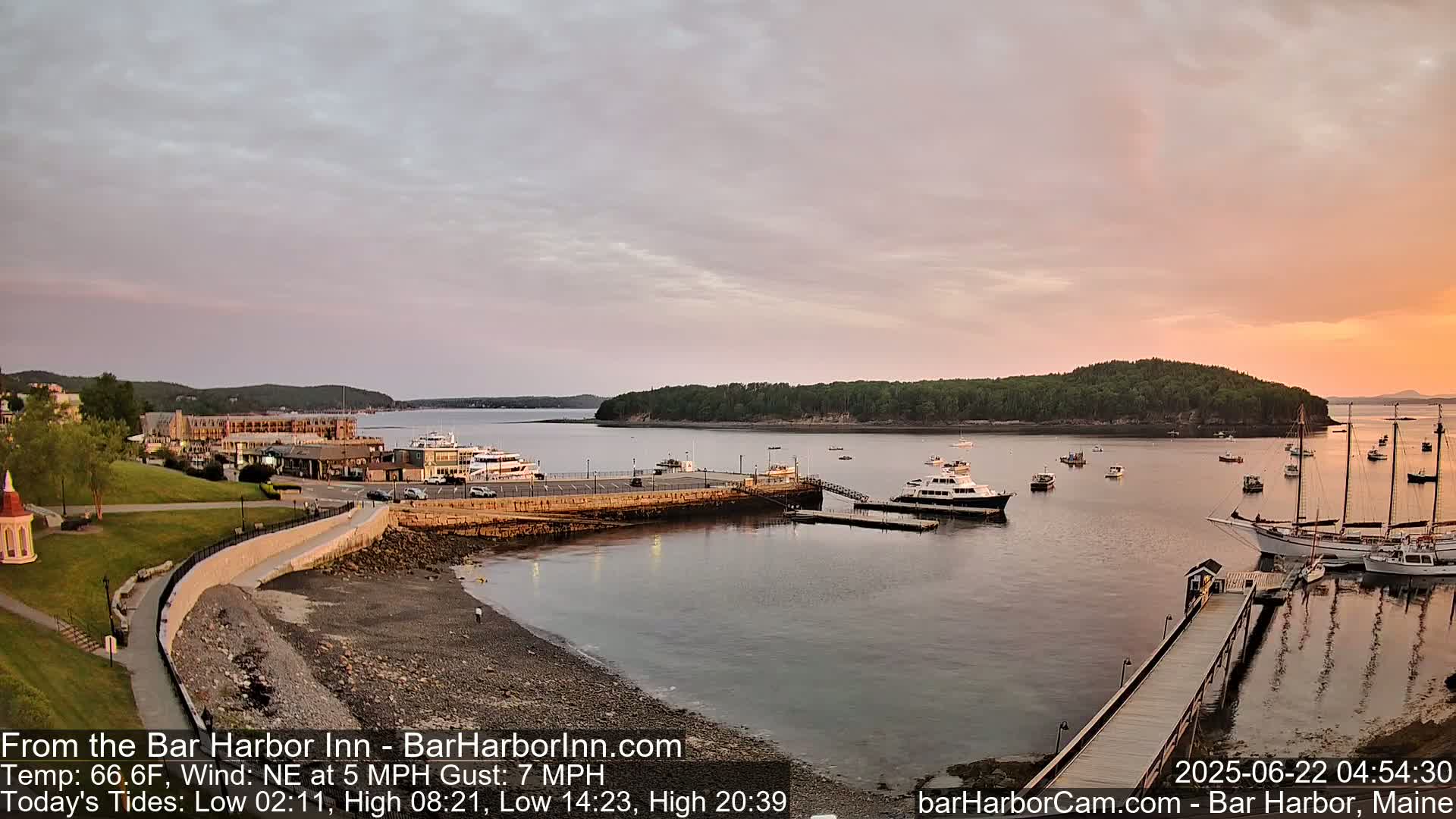 A calm harbor at sunset, with numerous boats docked and moored, and a large hotel visible in the background.