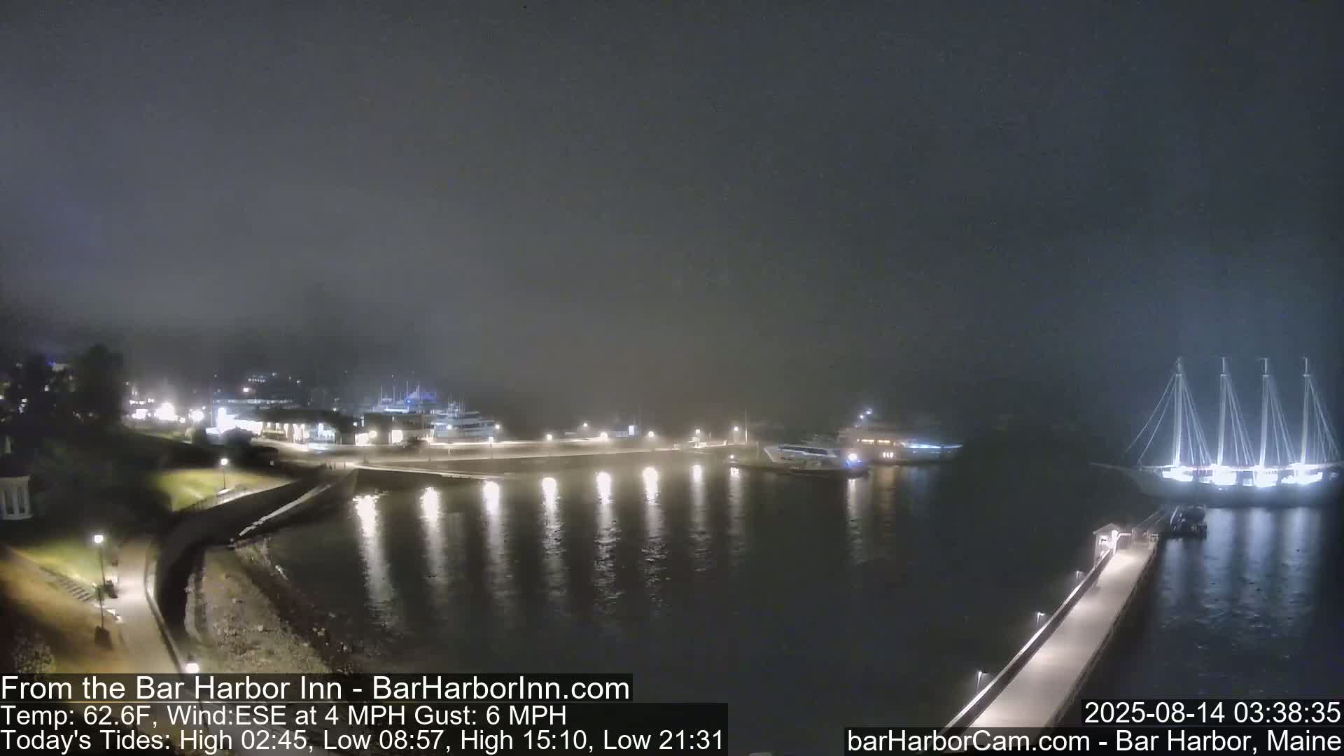 Several boats are moored in a harbor at night in foggy conditions.