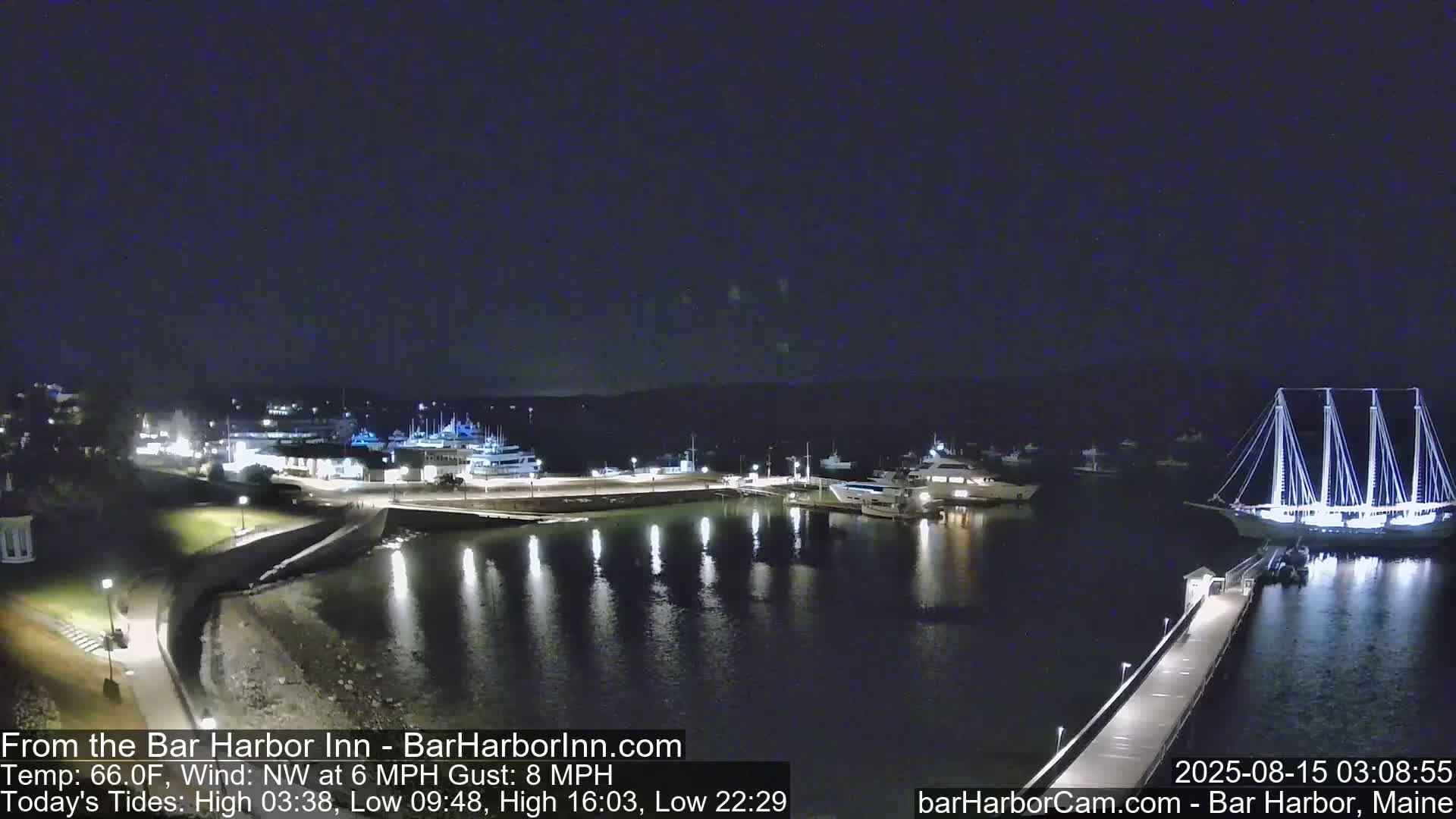 A nighttime harbor scene shows numerous boats docked, including a large, illuminated sailboat near a pier, under a dark, clear sky with a northwest wind.
