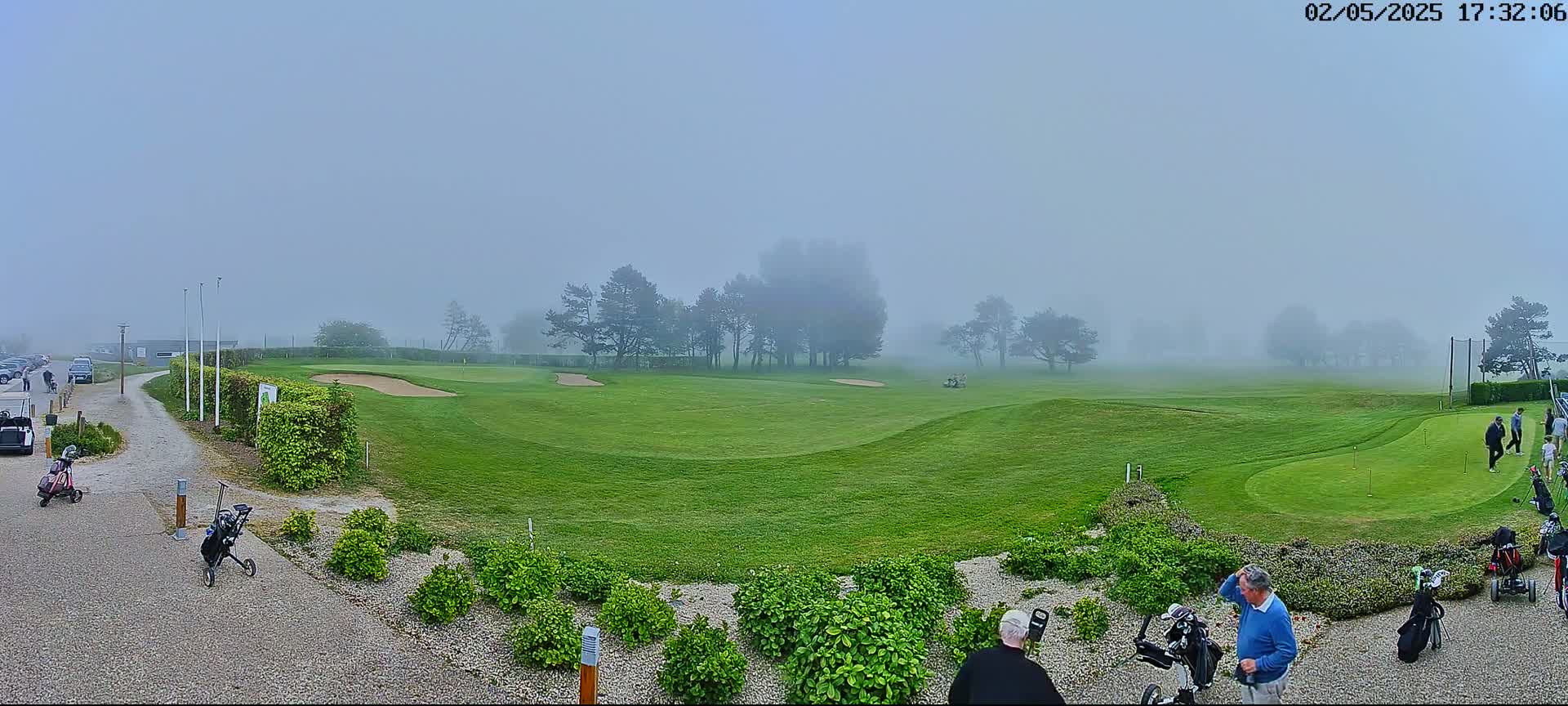 A foggy golf course with several people and golf carts near the clubhouse.