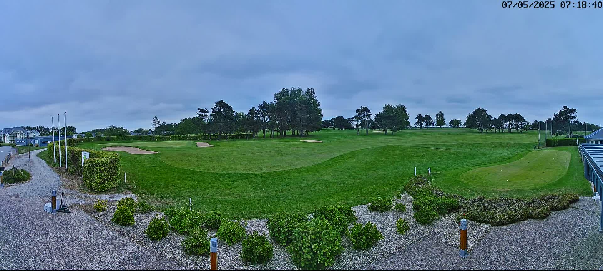 A panoramic view of a golf course on an overcast day, showing a green fairway with sand traps, lined with trees and landscaping.