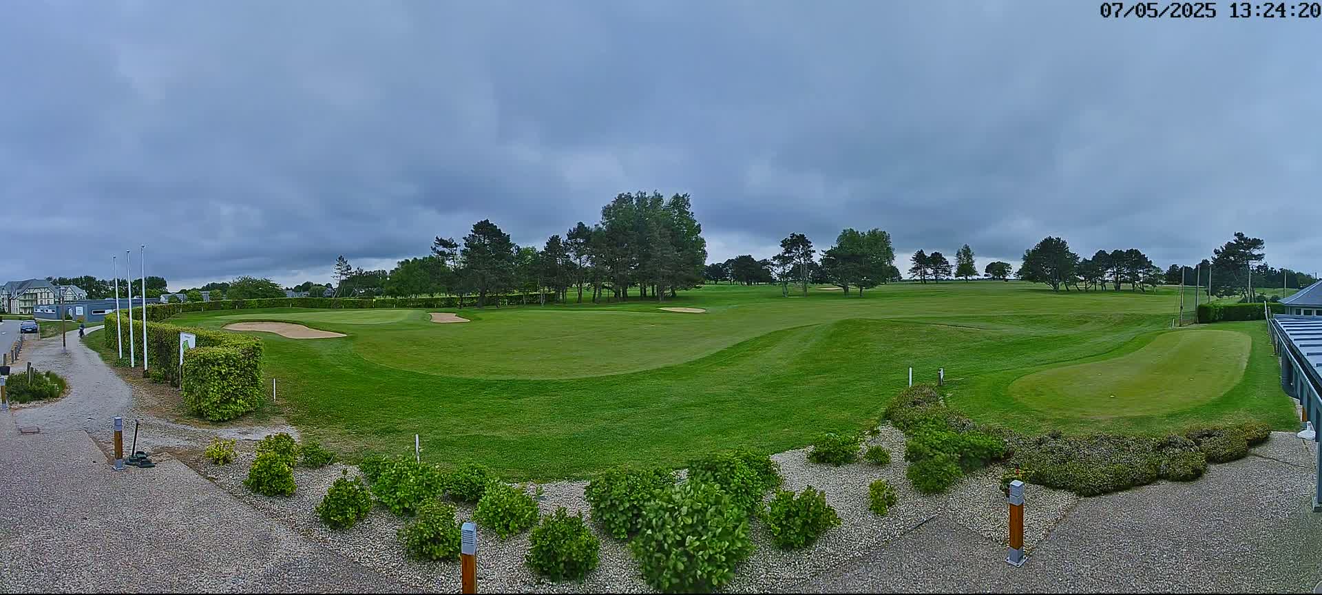 A green golf course with sand traps and several trees under a cloudy sky.