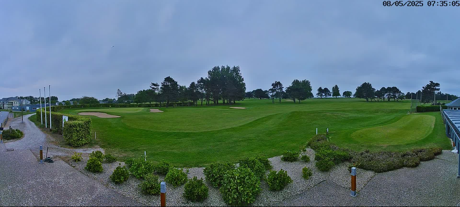 A golf course with green fairways, sand traps, and a putting green is visible under an overcast sky.