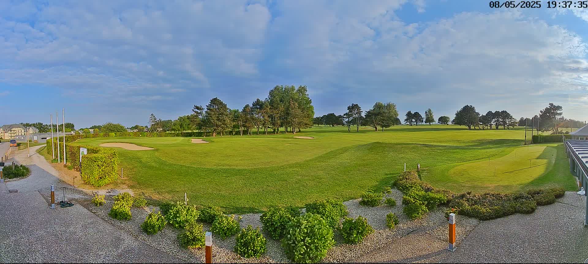 A golf course with green fairways and sand traps under a partly cloudy sky.