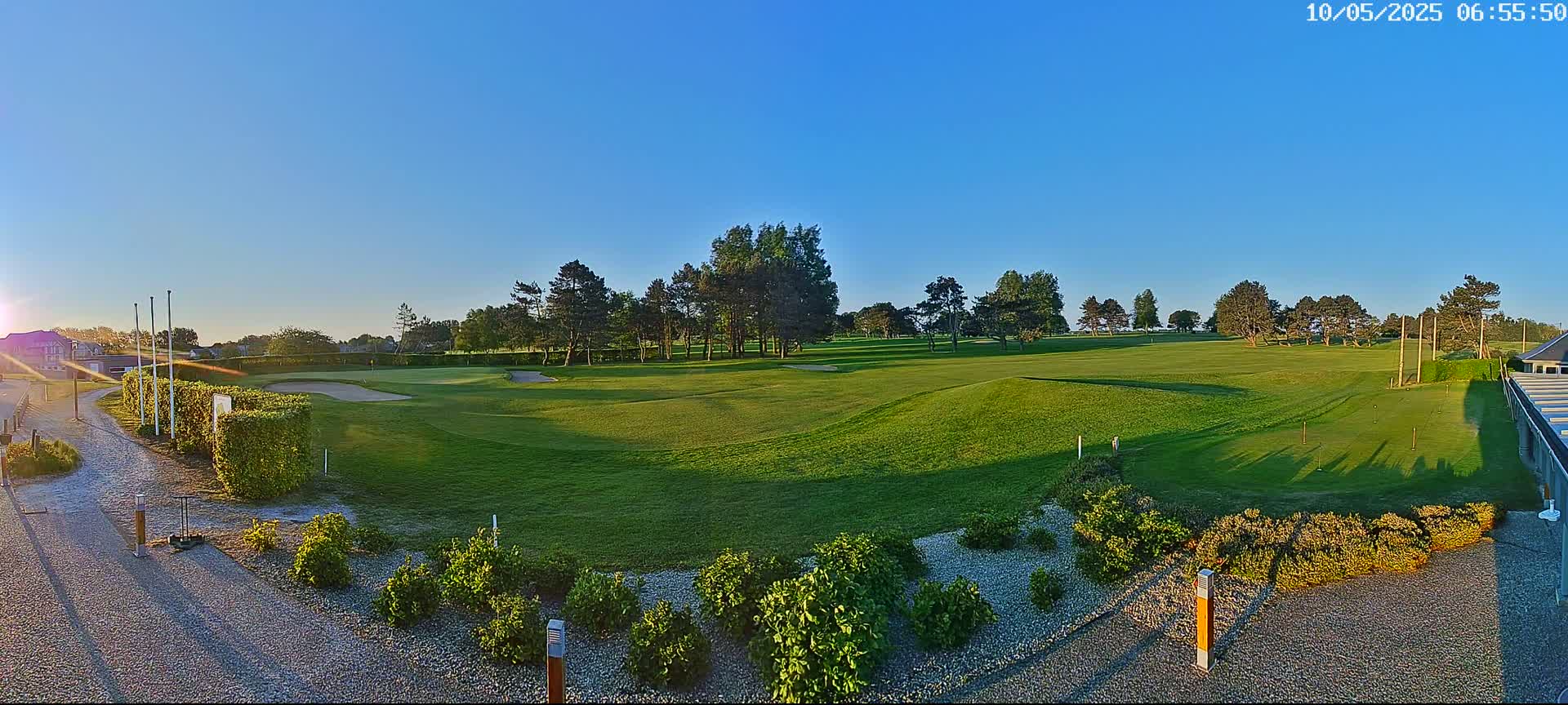 A sunny morning view of a golf course with green fairways, trees, and landscaping.
