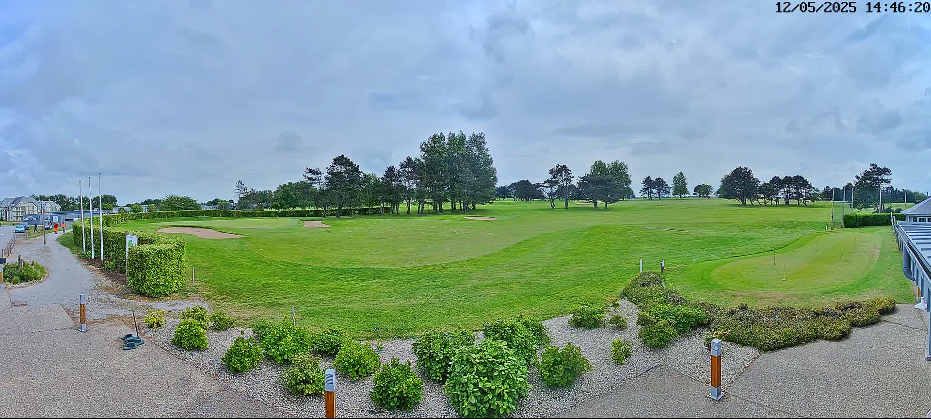 A green golf course with sand traps and neatly trimmed shrubs under a partly cloudy sky.