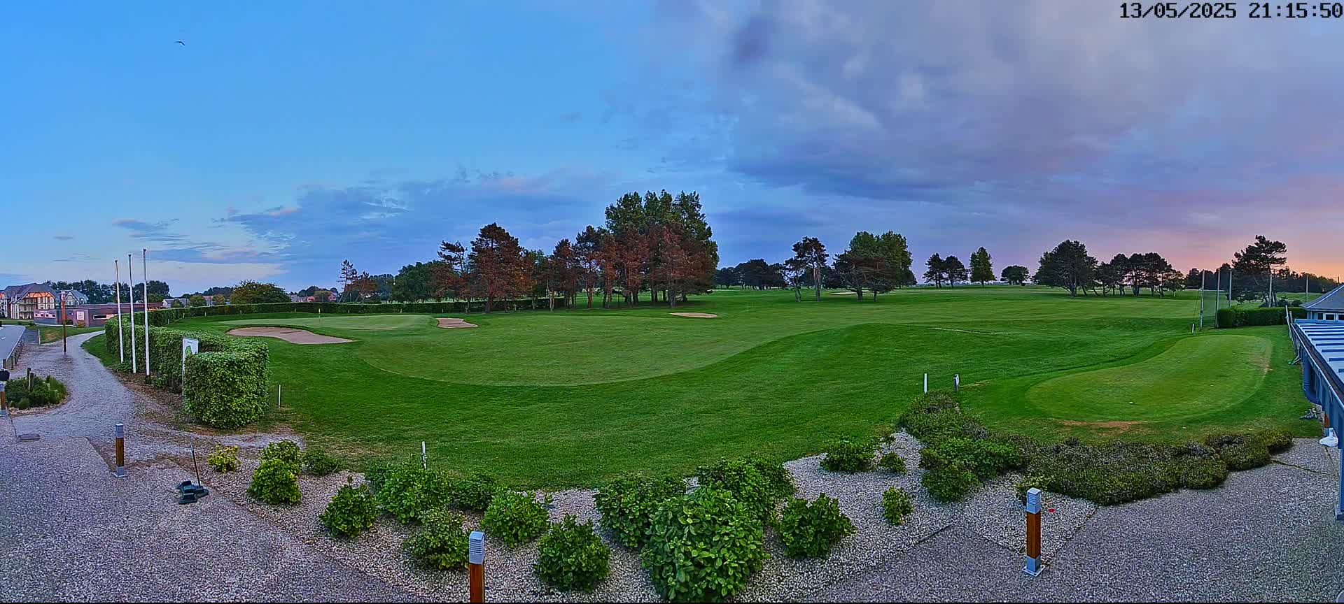 A golf course at dusk under a partly cloudy sky, with a building visible in the bottom right corner.