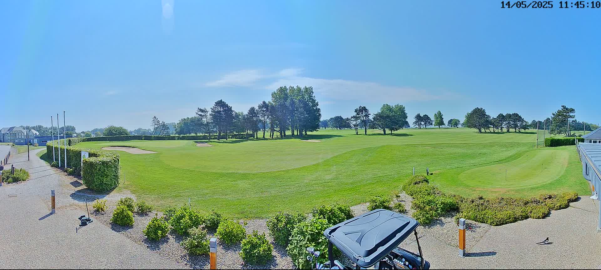 A golf course with green fairways, sand traps, and numerous trees under a clear blue sky.