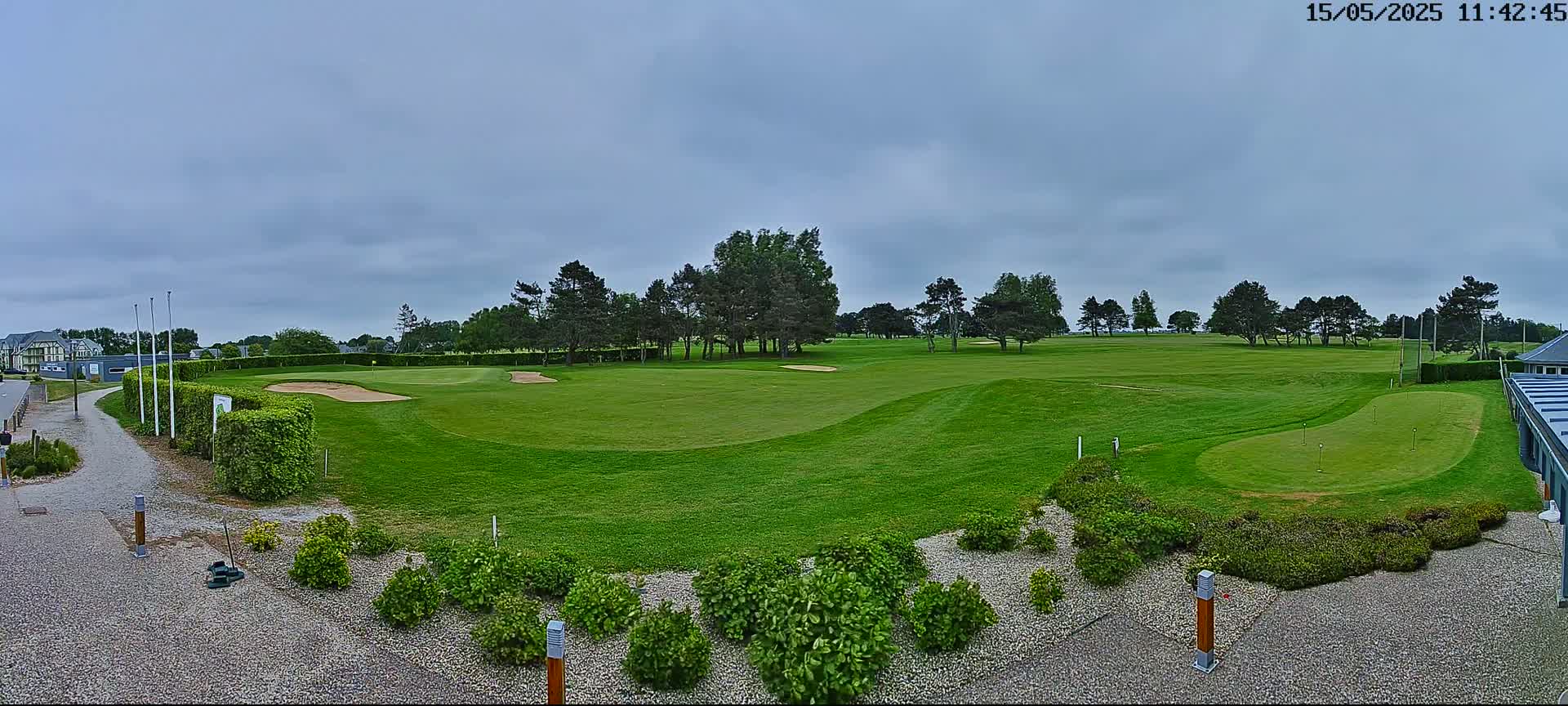 A green golf course with sand traps and trees under a cloudy sky.