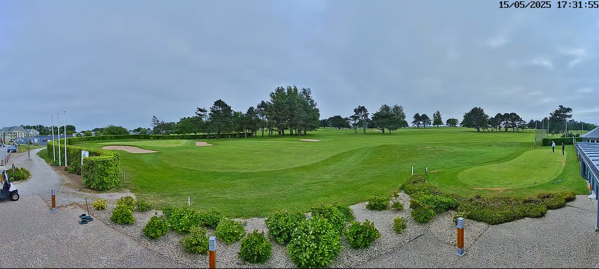 A golf course with green fairways, sand traps, and several trees under a cloudy sky.