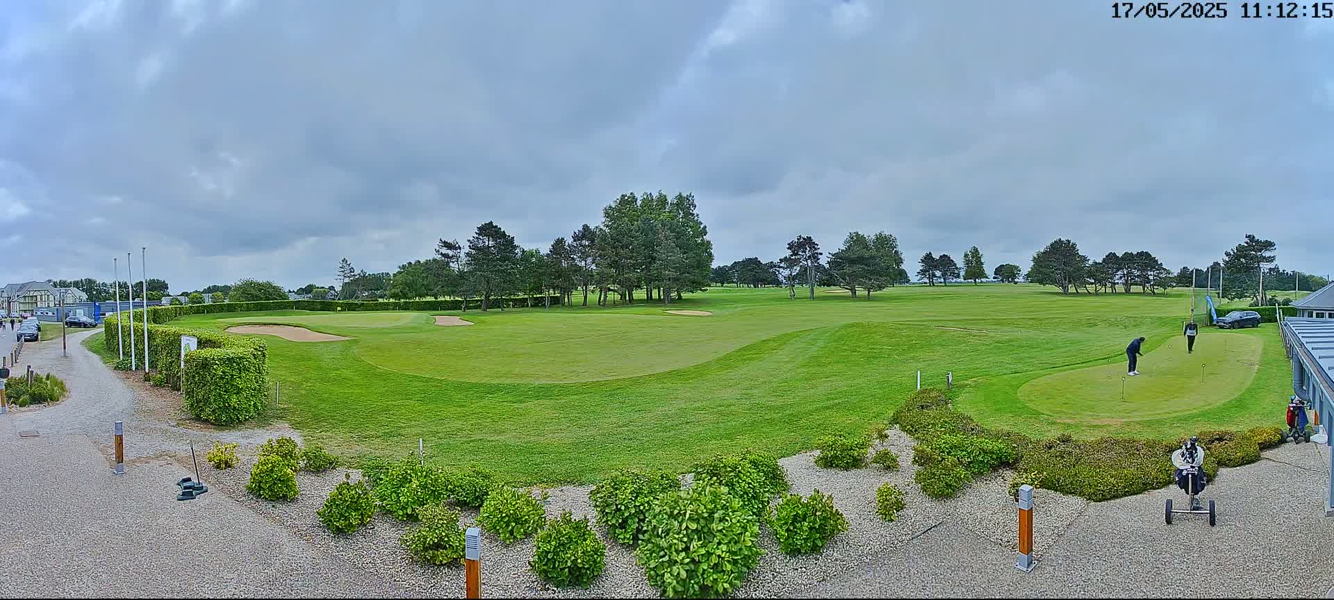 A golf course with two golfers on a putting green under a cloudy sky.