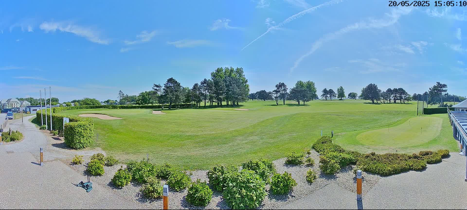 A sunny day shows a golf course with green fairways, sand traps, and putting greens, bordered by landscaping and trees.