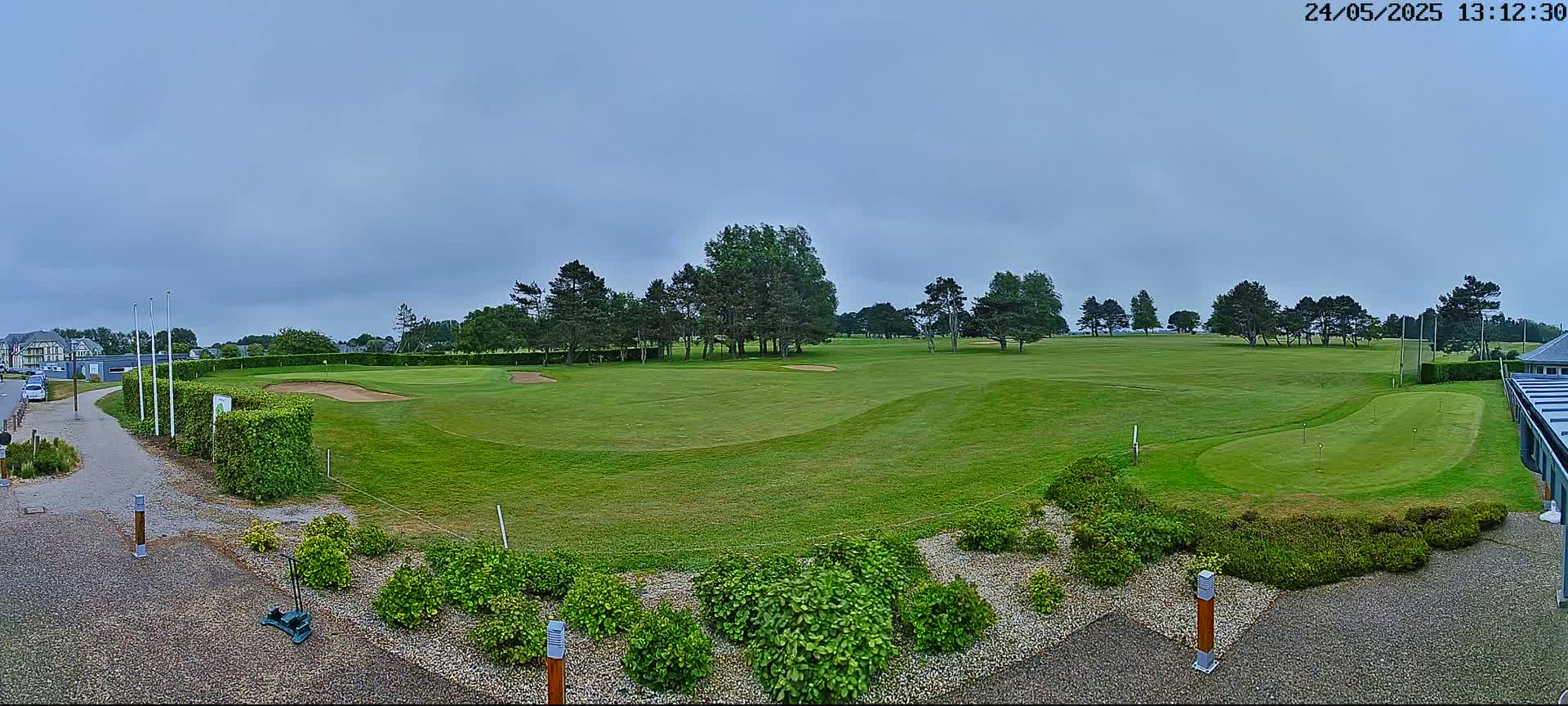 A green golf course with sand traps and several trees under a cloudy sky.