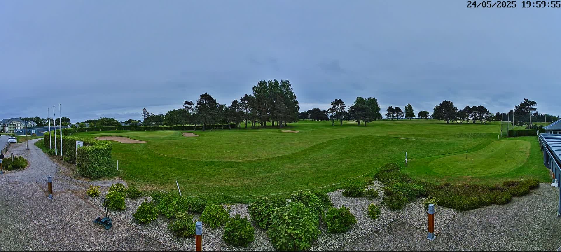A golf course with a putting green and sand traps is visible under an overcast sky.