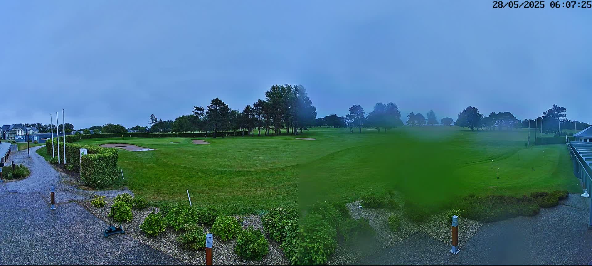 A golf course with green grass and trees is visible on an overcast day with light rain.