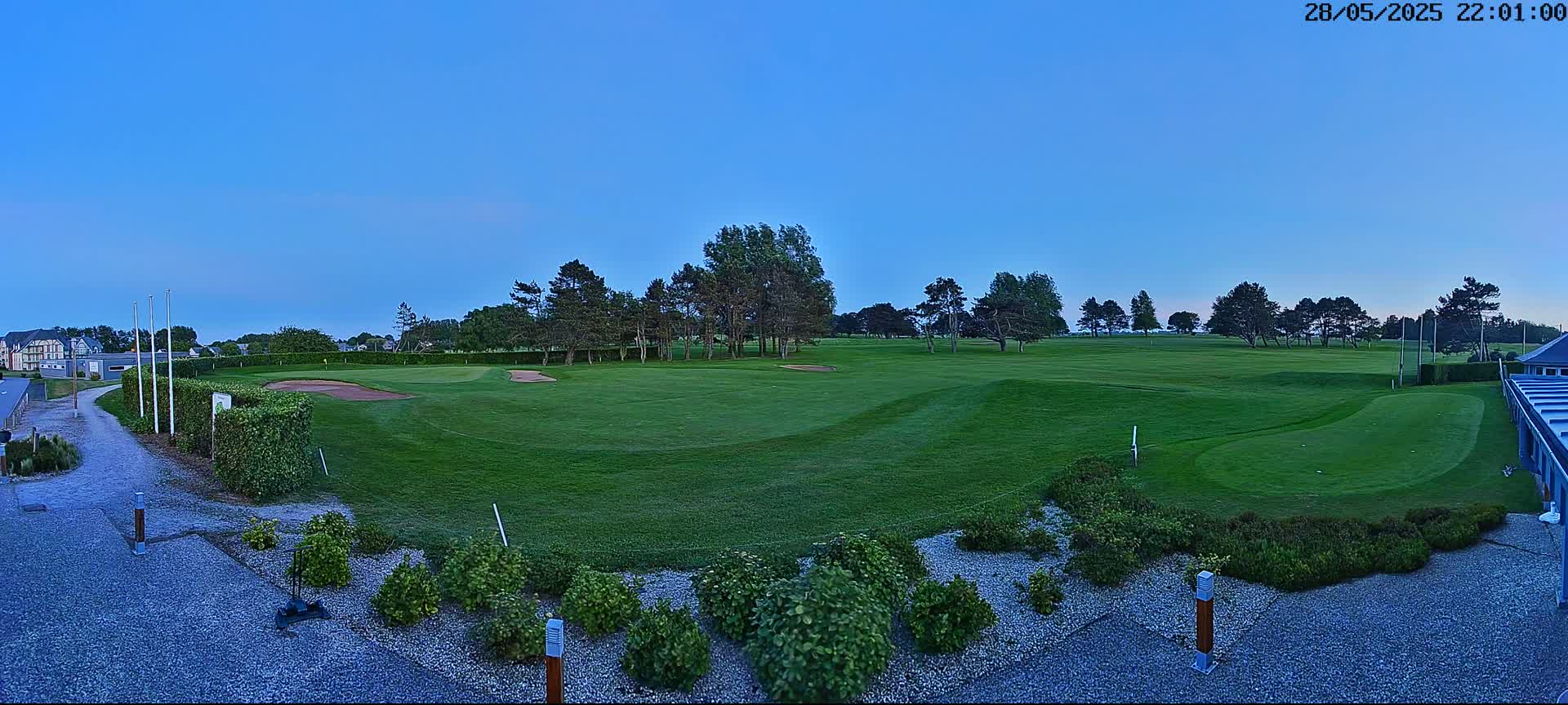 A mostly clear twilight sky illuminates a green golf course with sand traps, hedges, and landscaping.