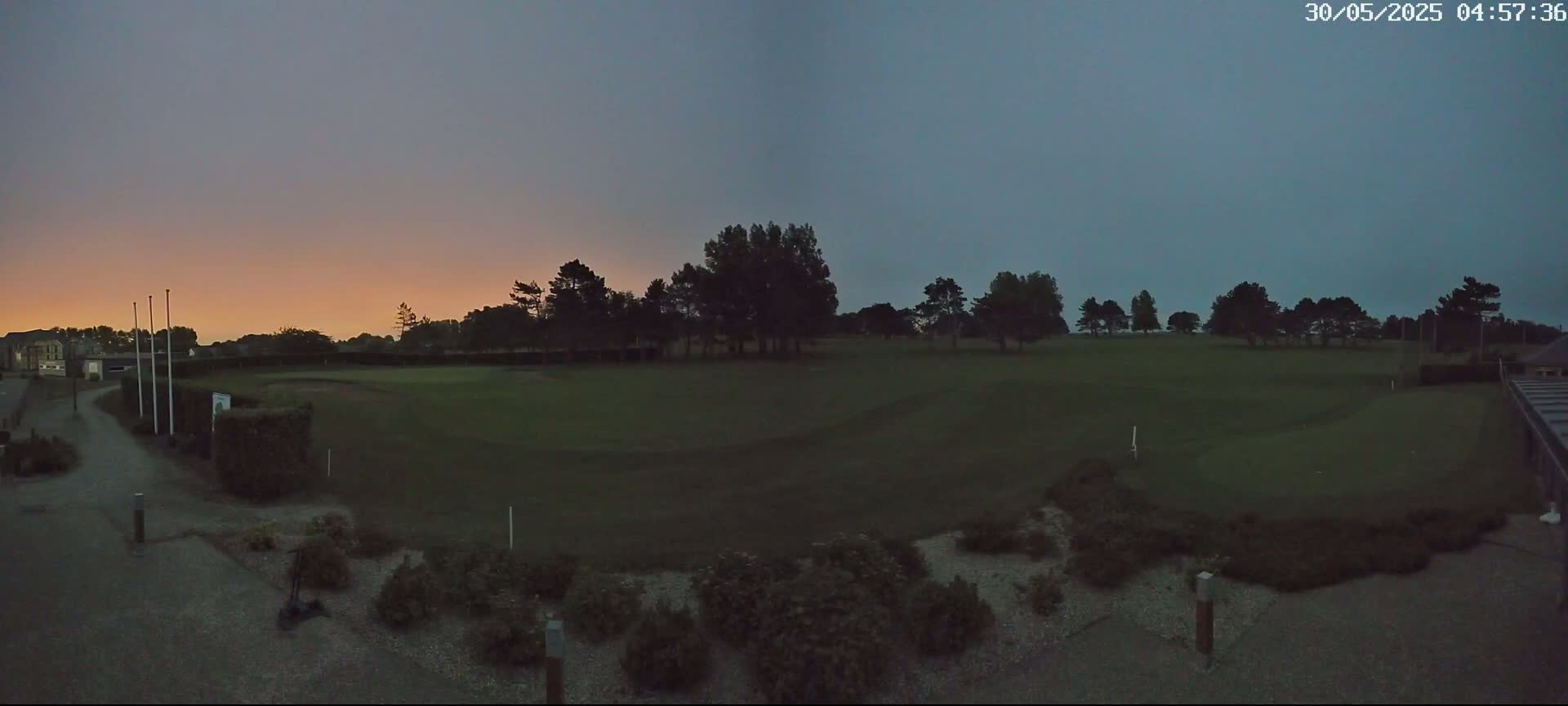 A twilight view of a golf course with a line of trees in the background under a dusky, orange-tinged sky.