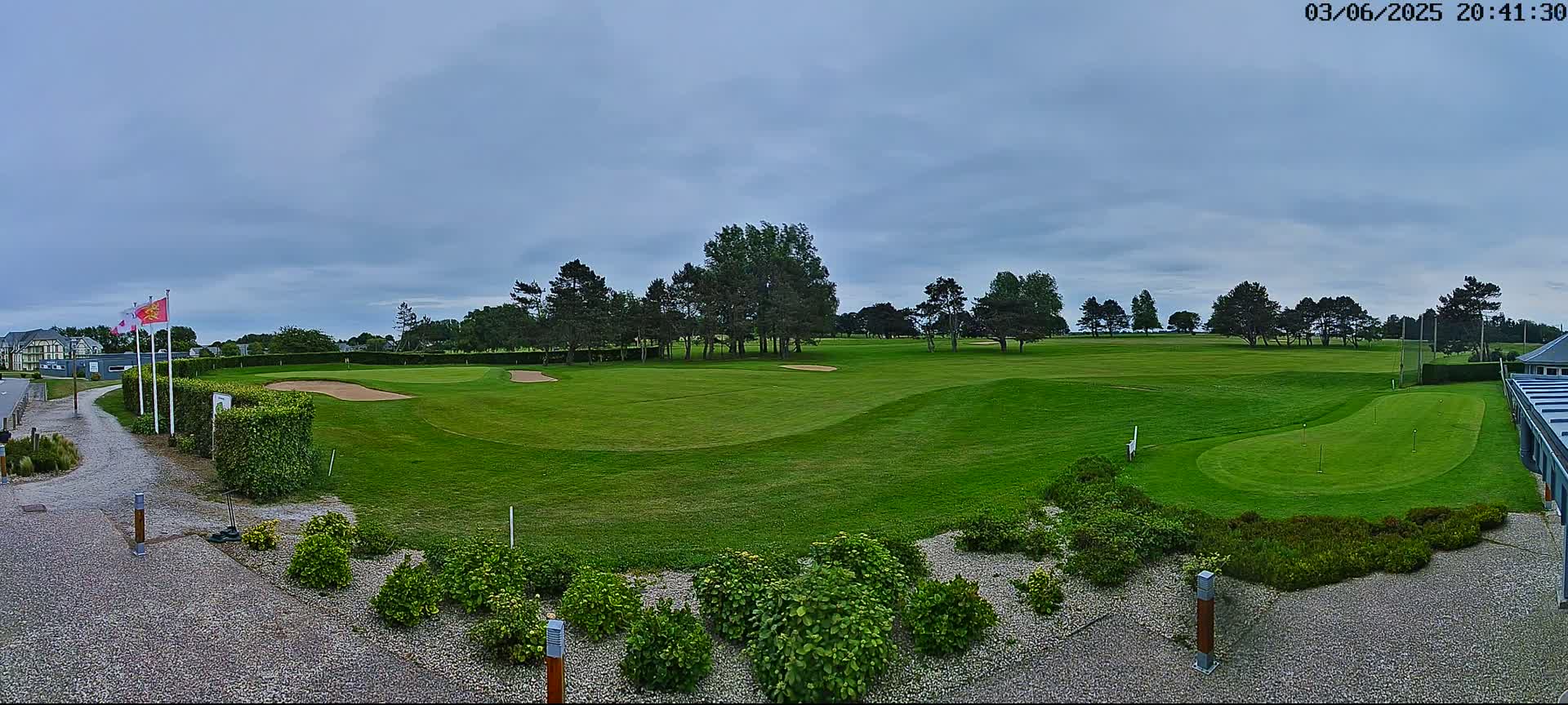 A golf course with putting greens and a line of trees under an overcast sky.