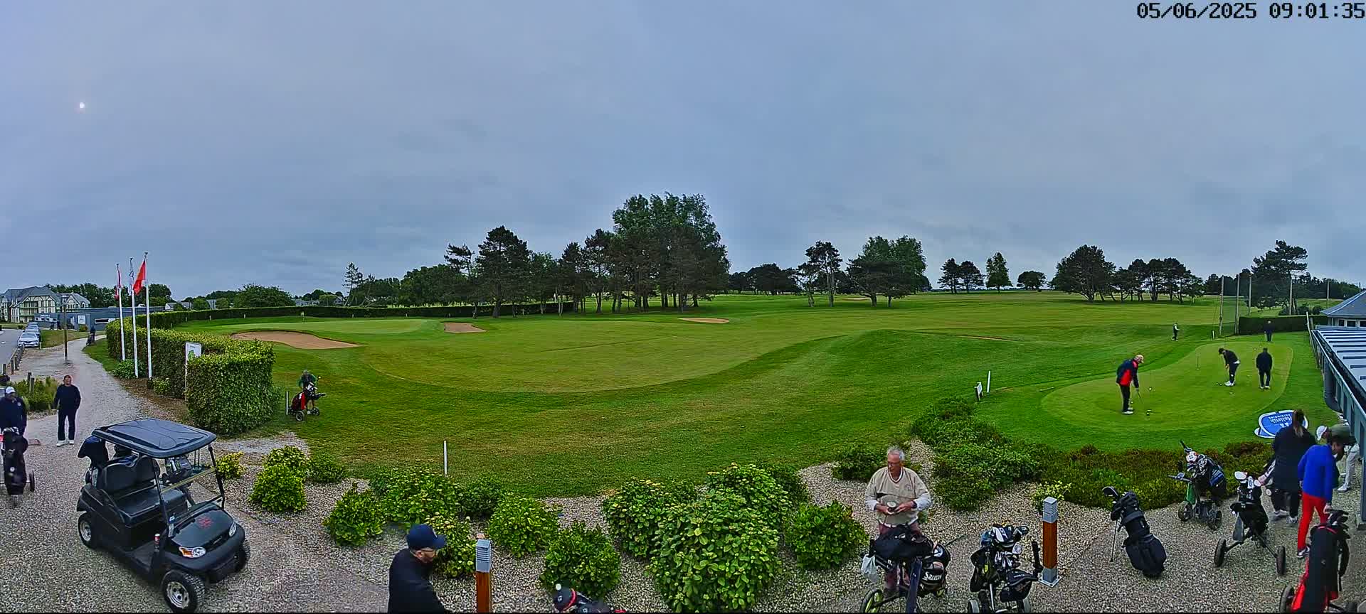 A golf course with several golfers on the green and putting area under an overcast sky.