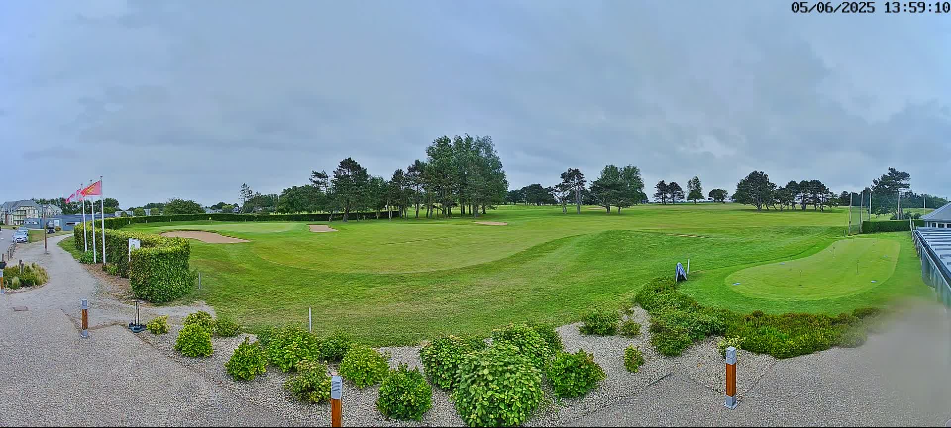 A golf course with green fairways, sand traps, and a putting green is visible under a cloudy sky.