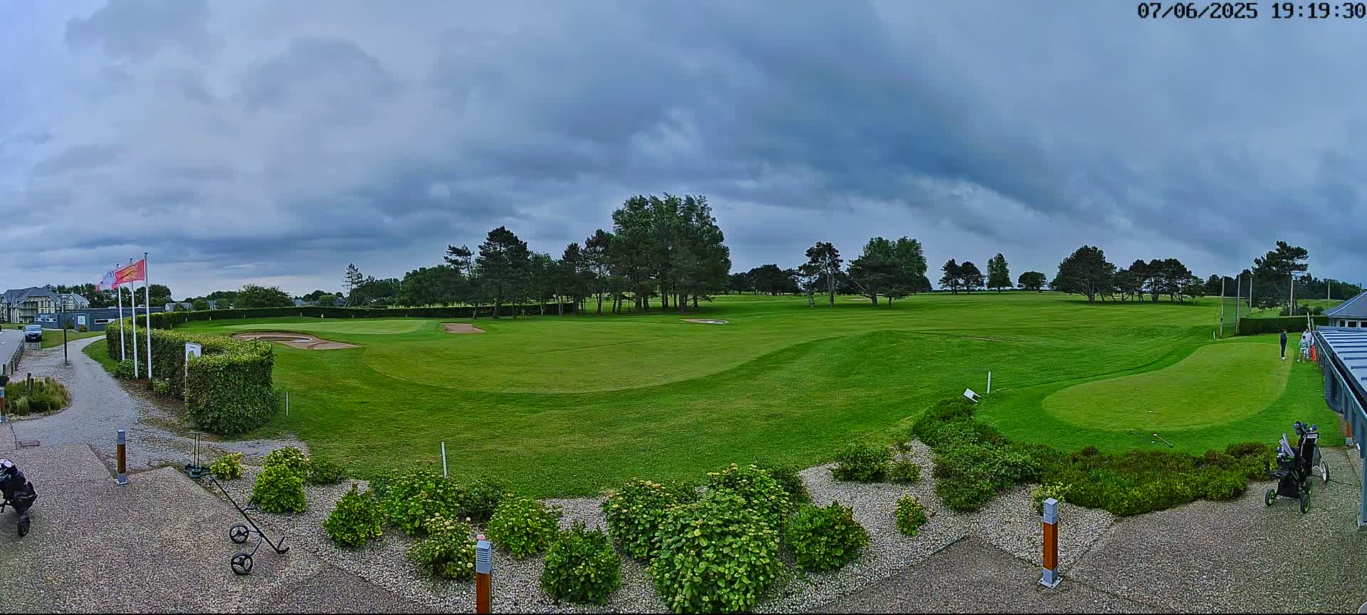 A golf course with a putting green and several golfers is visible under a cloudy sky.