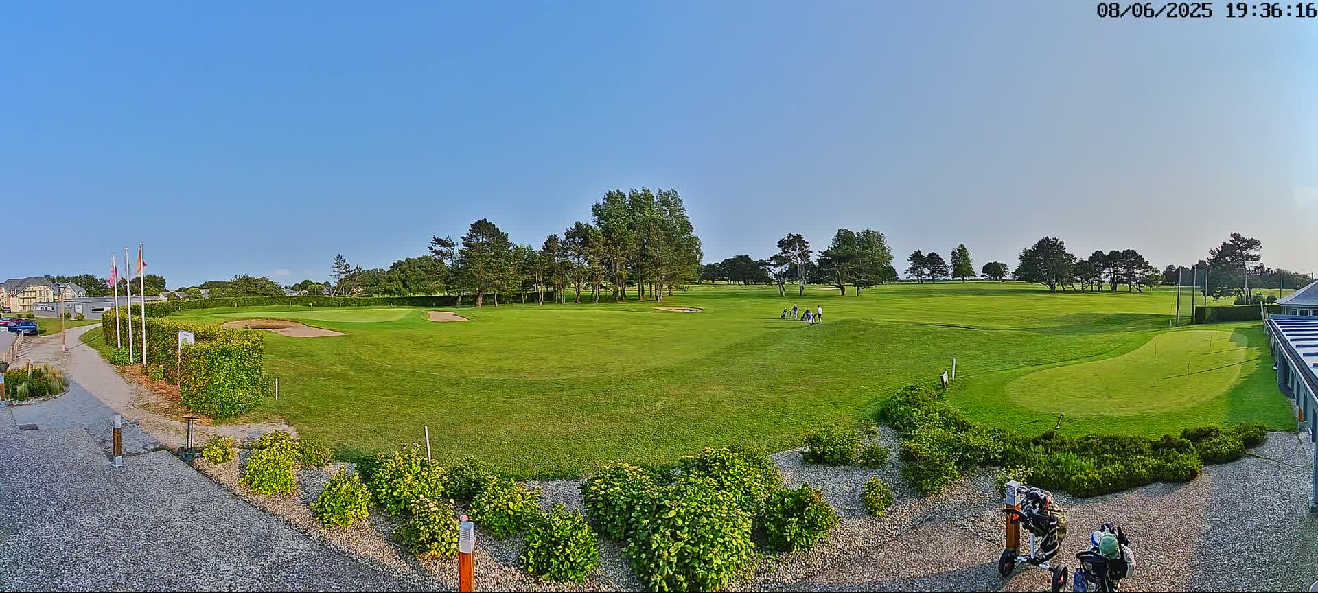 A golf course with several golfers on the fairway under a clear blue sky.