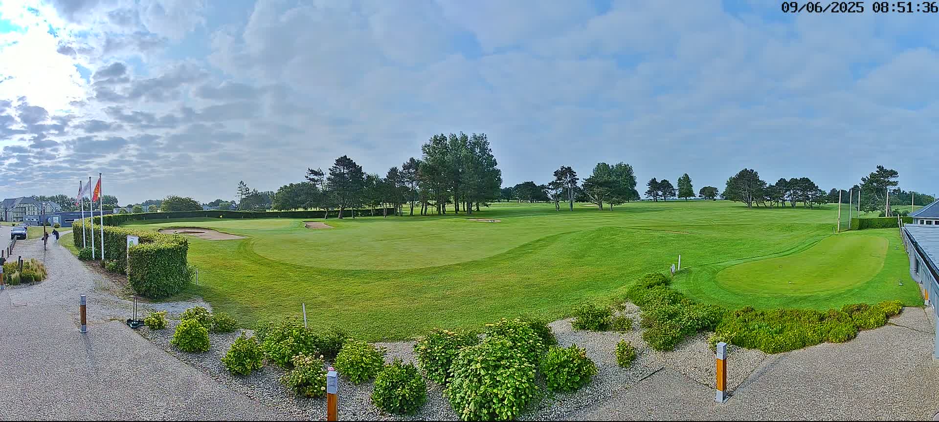 A partly cloudy sky overlooks a green golf course with several sand traps, trees, and landscaping.