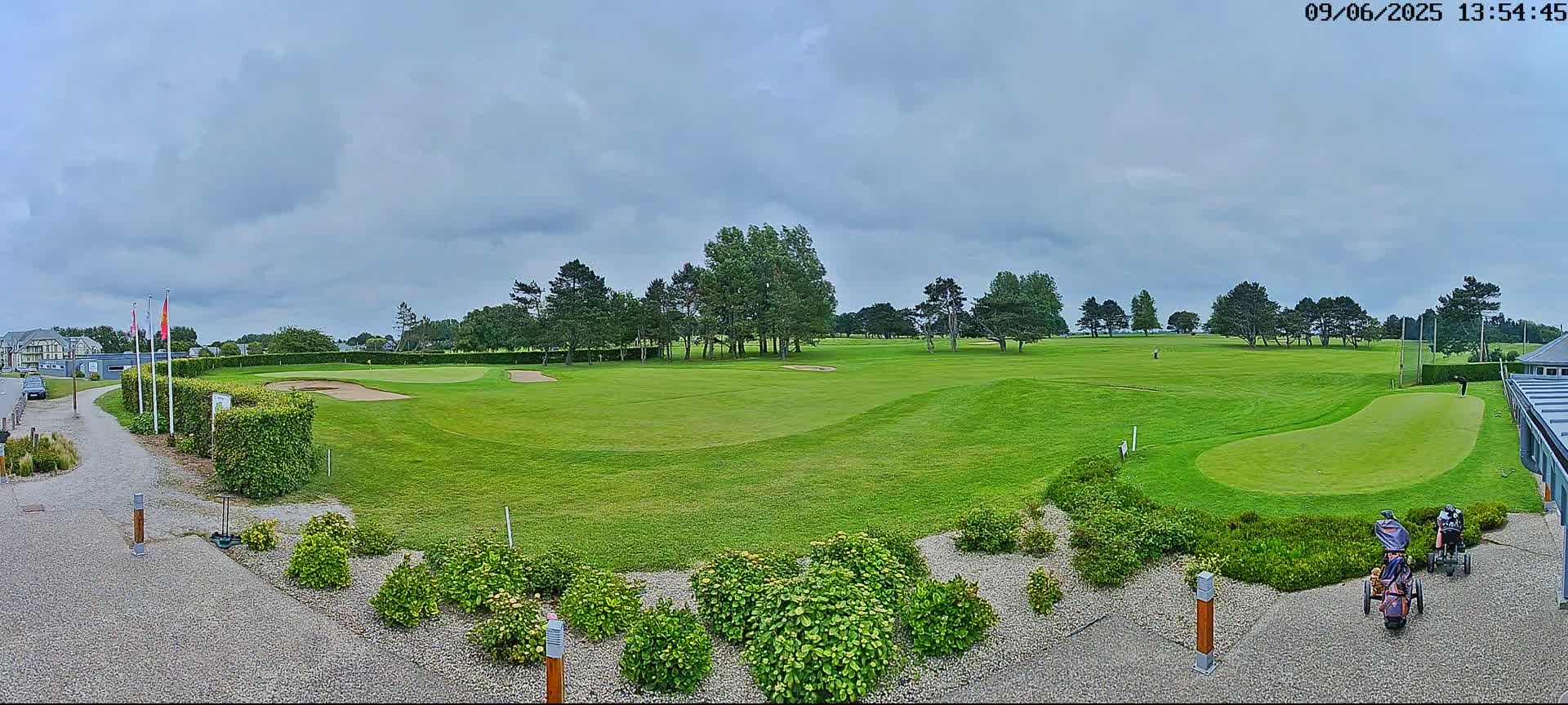 A golf course with green fairways, sand traps, and several golfers is viewed under a partly cloudy sky.