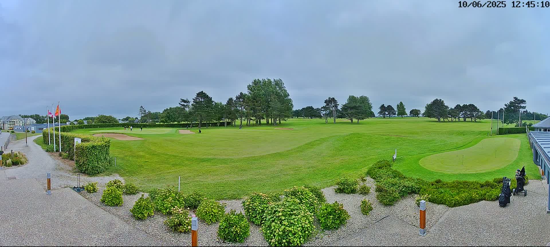 A golf course with several players visible on a mostly cloudy day.