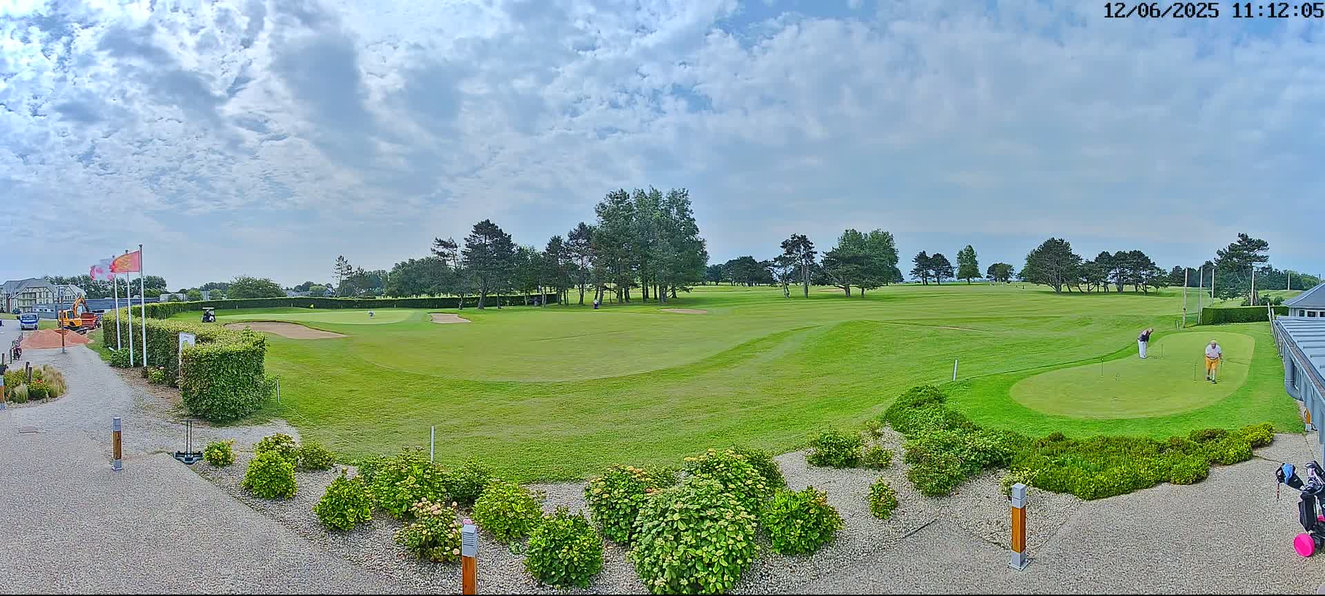 A golf course with two golfers on a putting green under a partly cloudy sky.