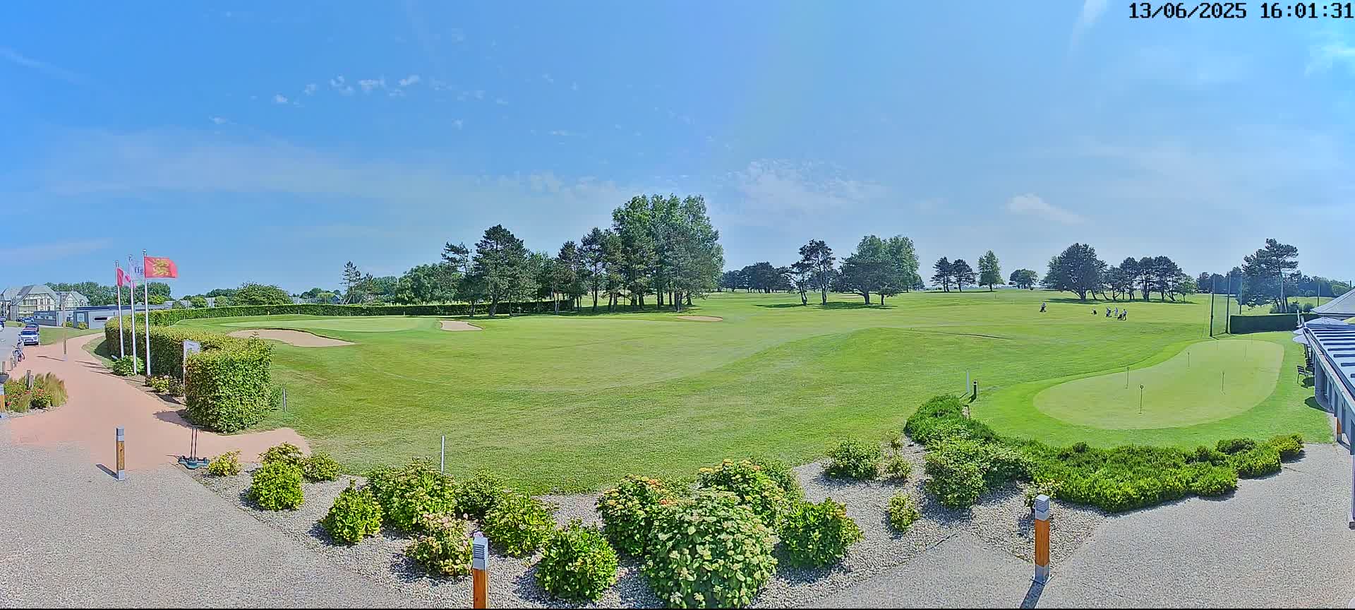 A sunny day reveals a golf course with players visible on the green, surrounded by lush greenery and a paved walkway.