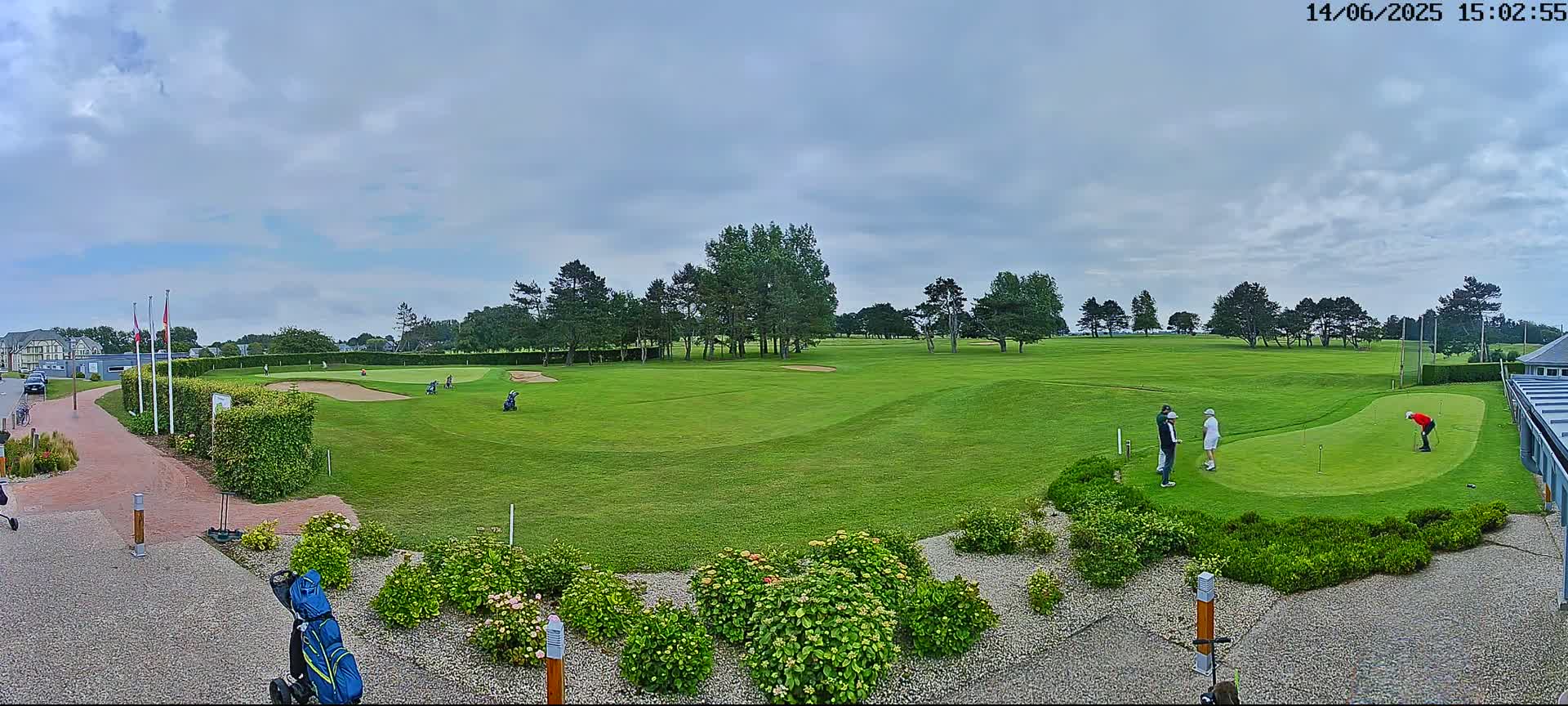A golf course with several golfers visible on a partly cloudy day.