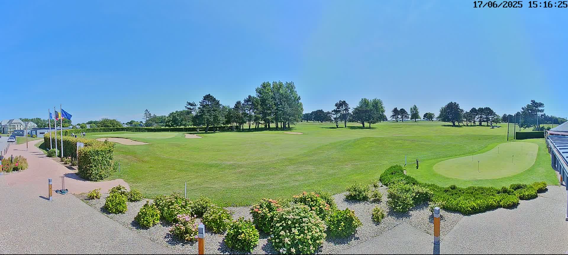 A sunny day on a golf course shows a putting green, a fairway, and landscaping near a building.
