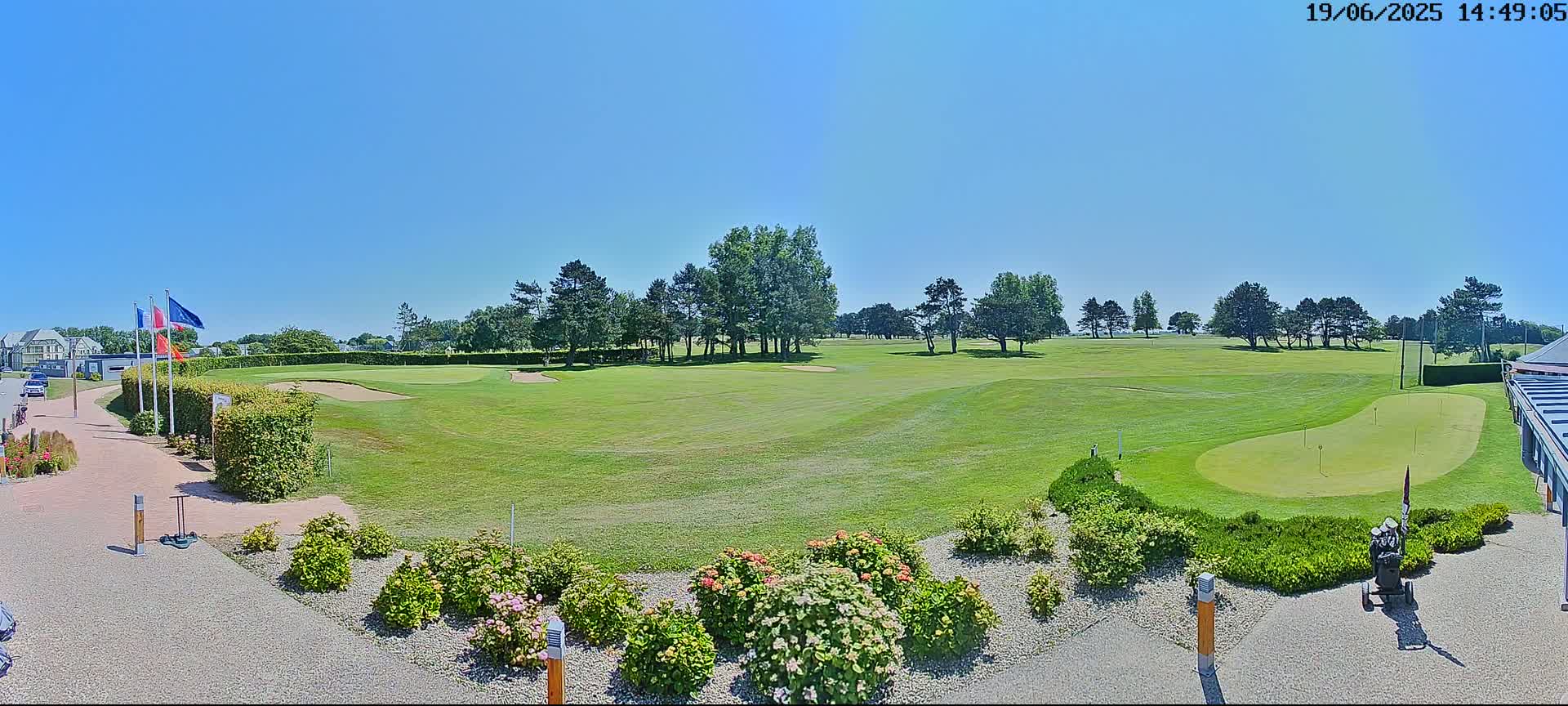 A sunny day reveals a golf course with green fairways, sand traps, and putting greens, surrounded by landscaping and trees.