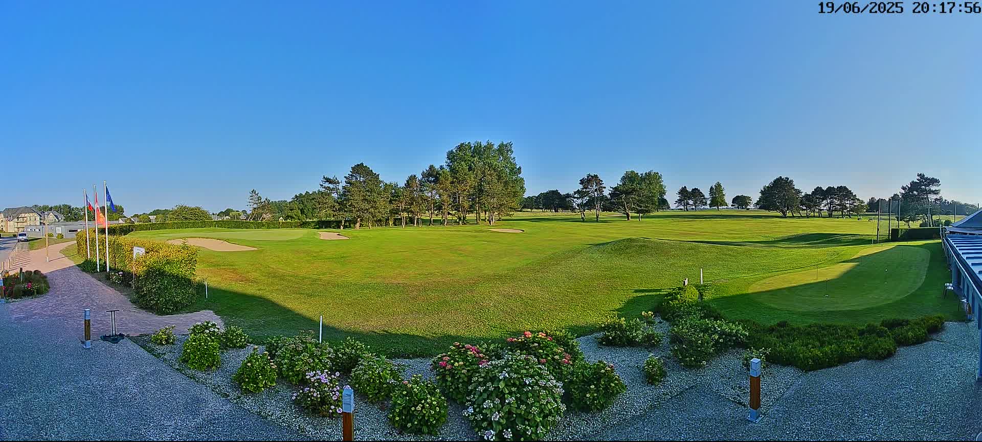 A sunny day reveals a lush green golf course with several sand traps, bordered by trees and colorful landscaping.
