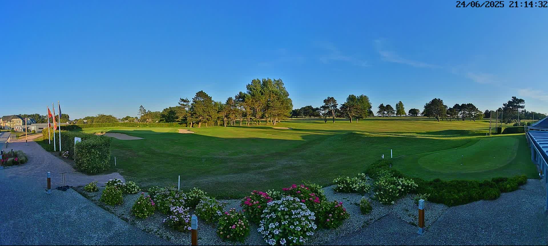 A green golf course with trees and flowerbeds, under a clear blue sky.