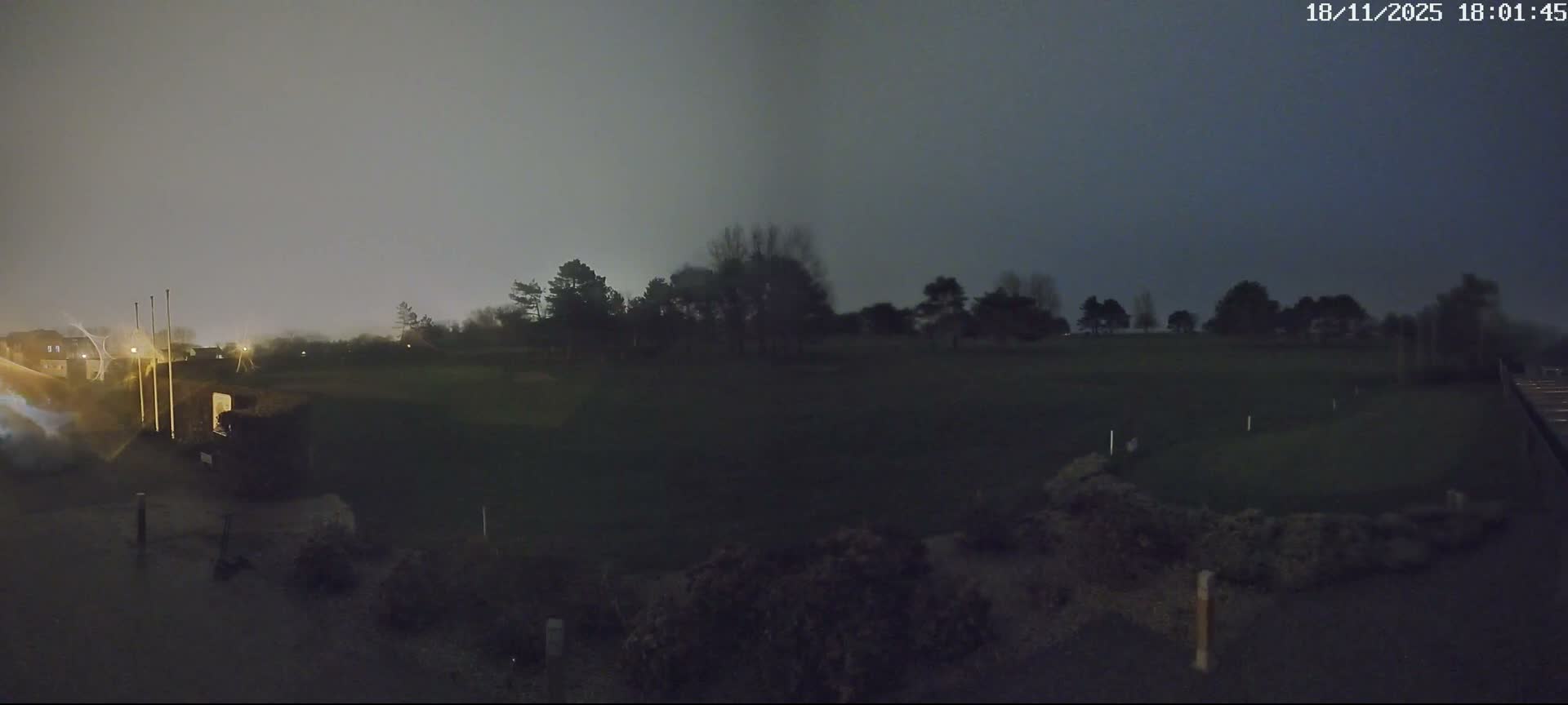 A sunny day reveals a golf course with green fairways, trees, and vibrant pink flowers in the foreground.