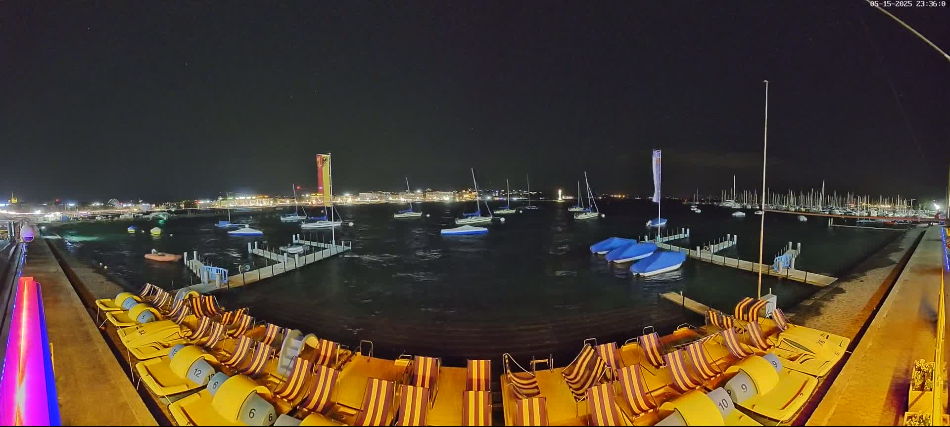 At night, a body of water with sailboats and pedal boats is shown under a dark, clear sky.