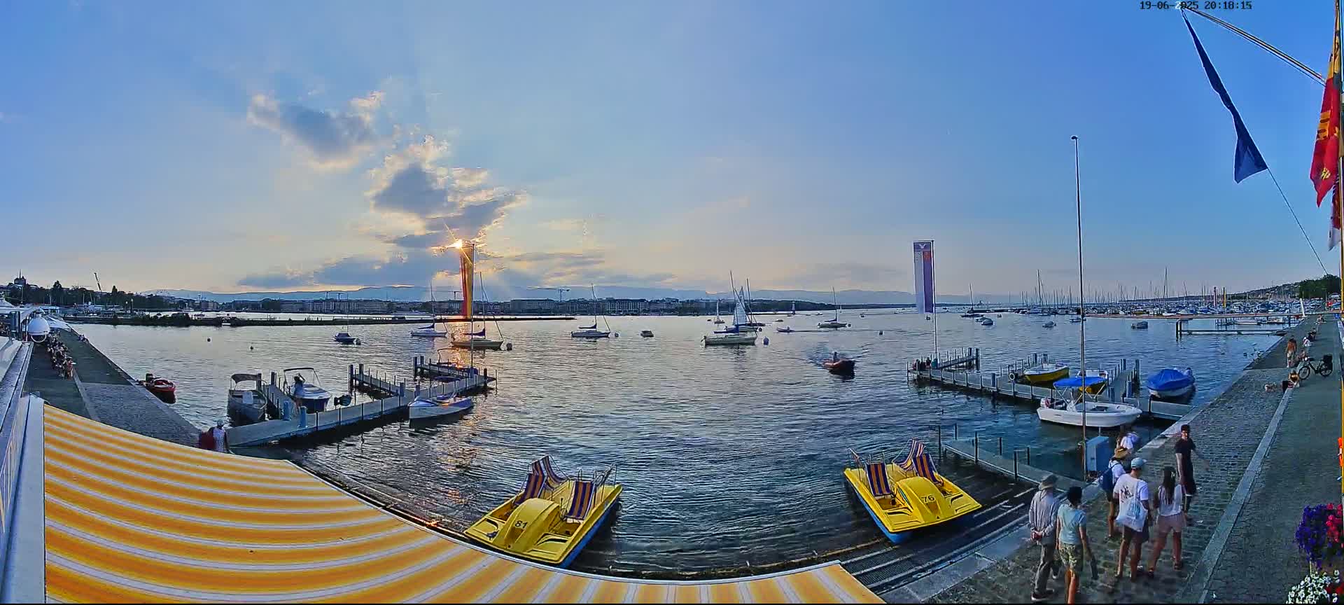 A calm lake at sunset, with numerous boats and people gathered near a dock.