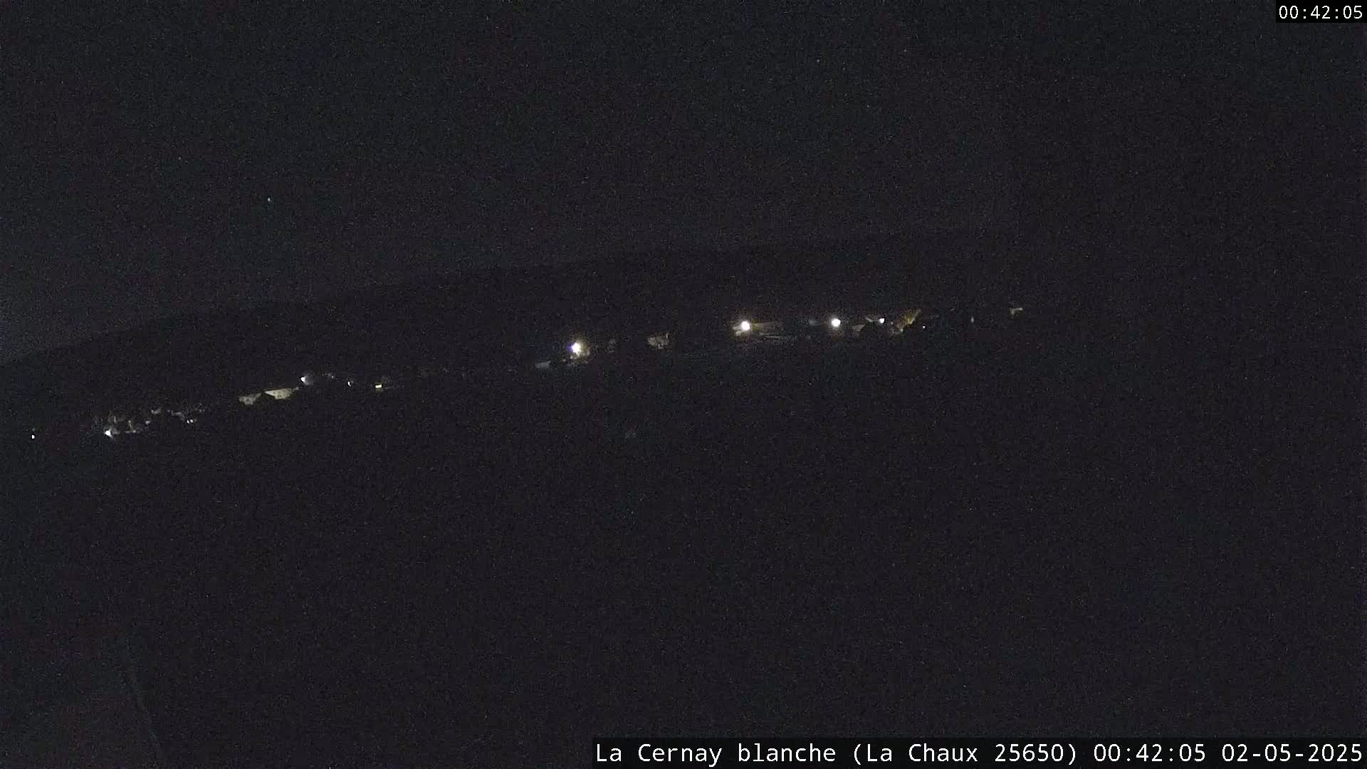 A nighttime, long-range view shows a line of dimly lit buildings or structures under a dark sky.