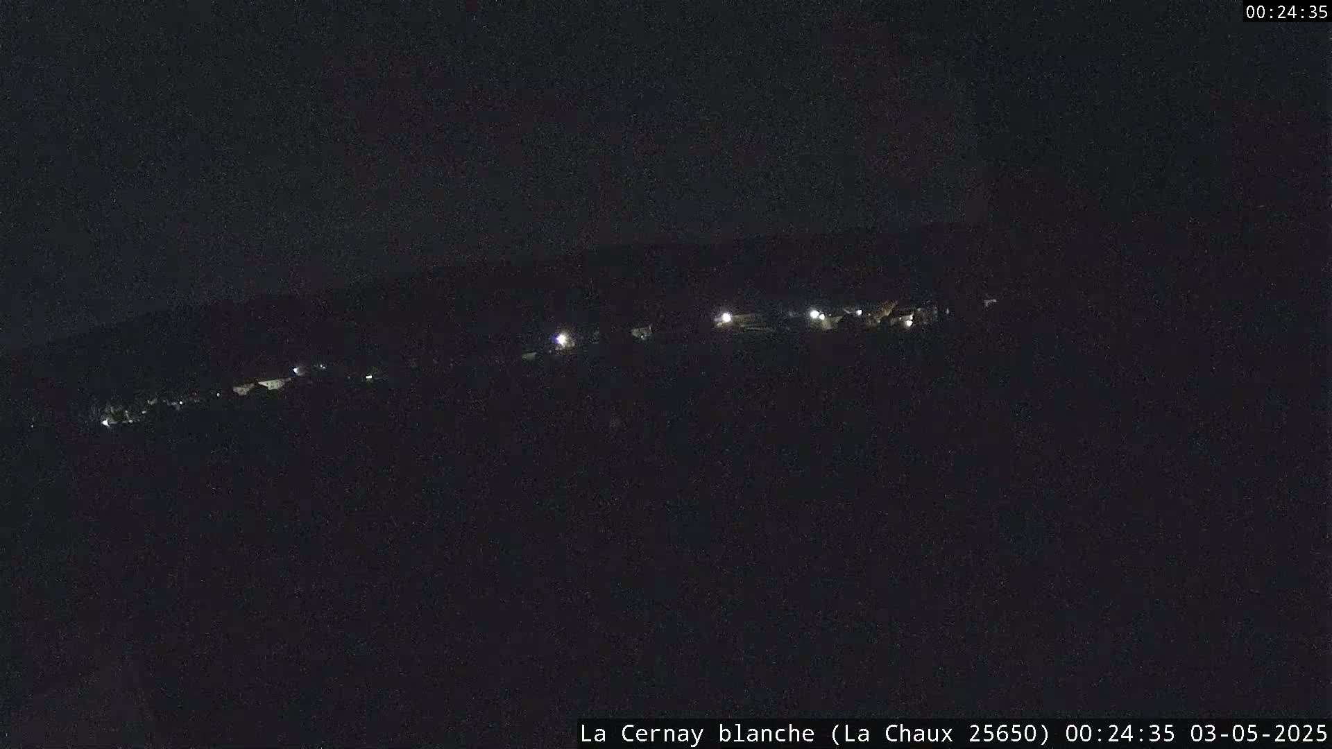 A dark, nighttime scene shows a line of faint lights in the distance on a hill.