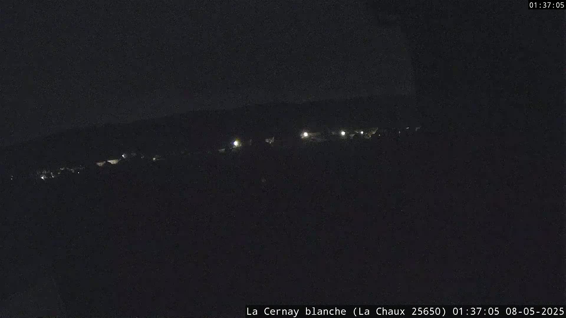 A nighttime, long-range view shows a dark landscape with a few faint lights in the distance.