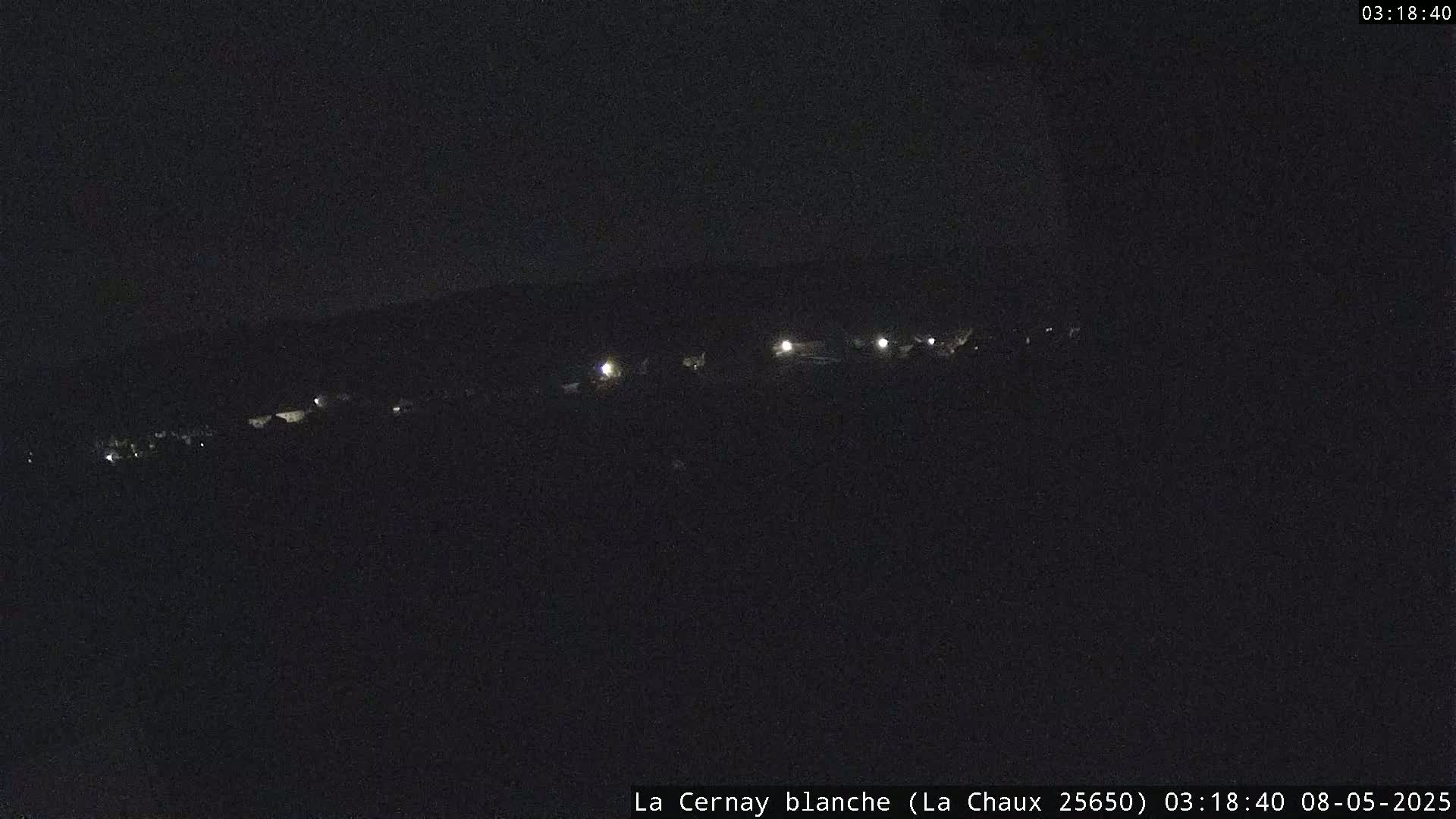 A nighttime, long-range view shows a few faint lights in the distance on a dark landscape.