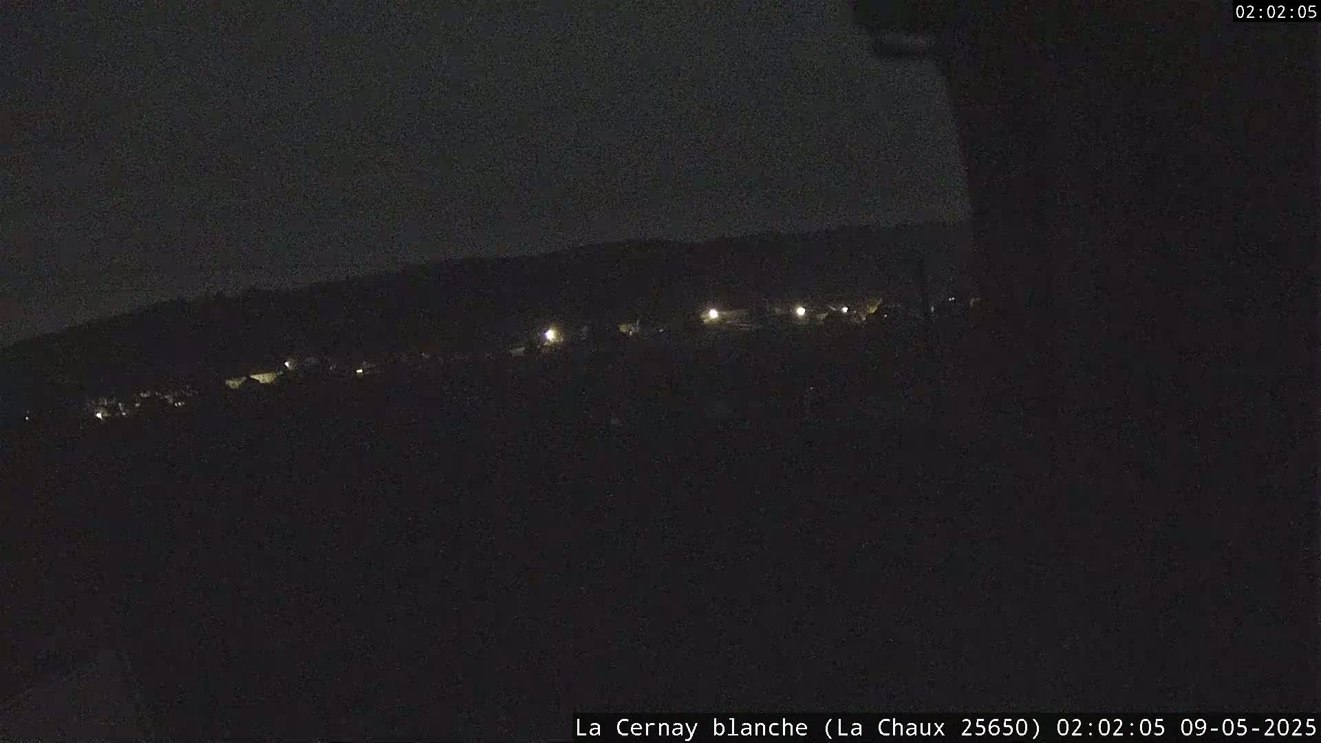 A nighttime, dark view of a distant line of faintly lit structures in a dark landscape.
