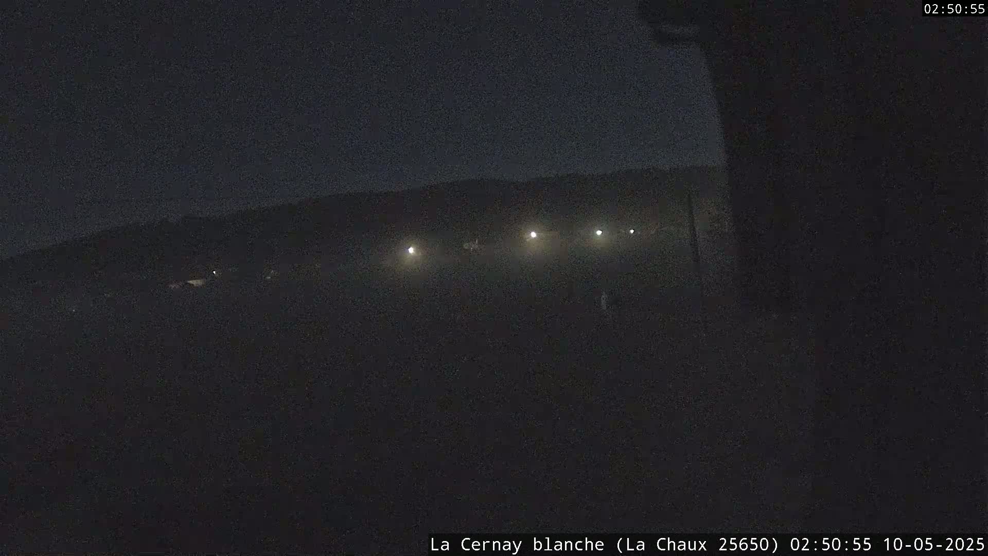 A dark, nighttime scene shows a flat, dimly lit landscape with a few distant lights.