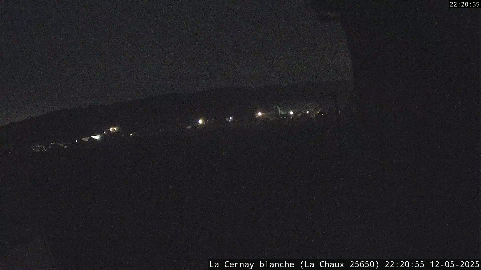 A dark, nighttime view of a distant, dimly lit town or village under a clear sky.